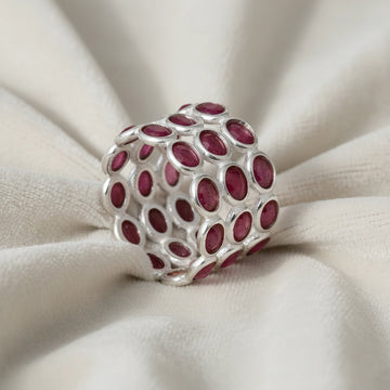 Wide silver ruby band ring featuring three tiers of dark oval rubies mounted on textured white cloth with side profile.
