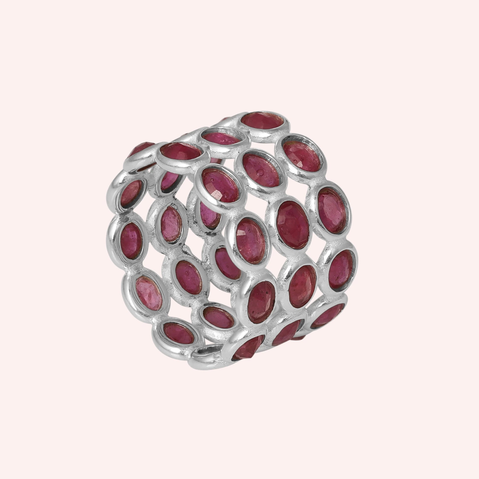 Silver ruby eternity band ring featuring large oval-cut rubies in an open basket setting against a soft pink background side angle.