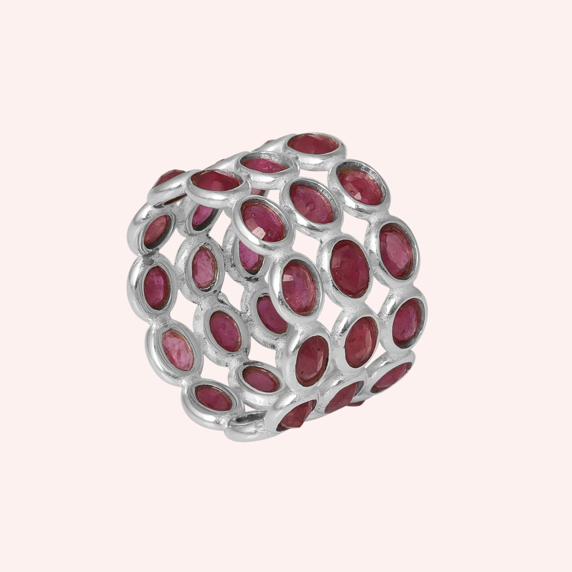 Silver ruby eternity band ring featuring large oval-cut rubies in an open basket setting against a soft pink background side angle.