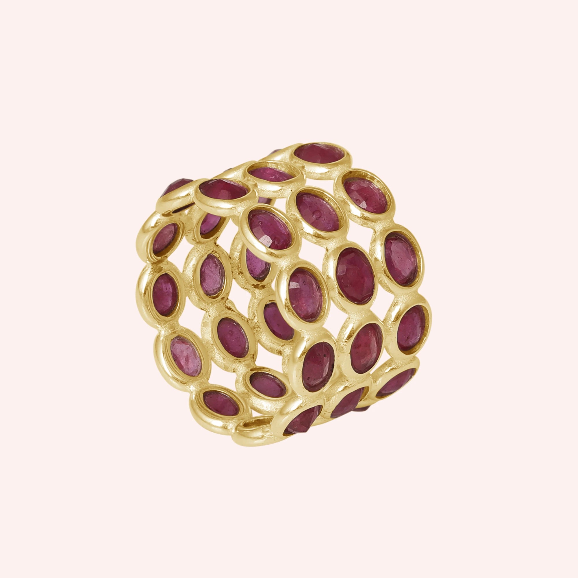 Wide gold ruby eternity ring band featuring oval-cut rubies in an open setting on a pink background from a strong side angle.