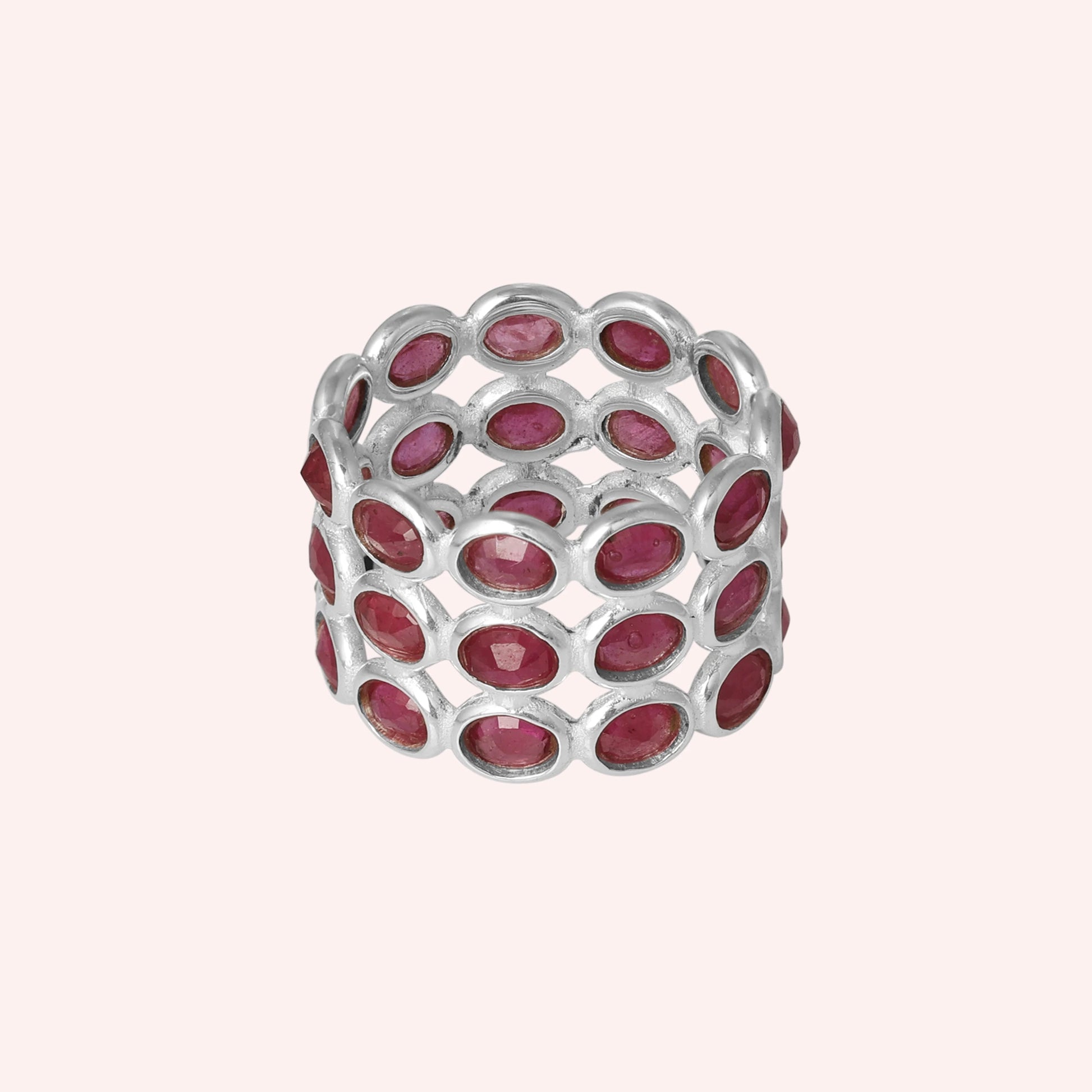 Wide silver ruby eternity ring band featuring oval-cut rubies in an open setting on a pink background from a direct front angle.