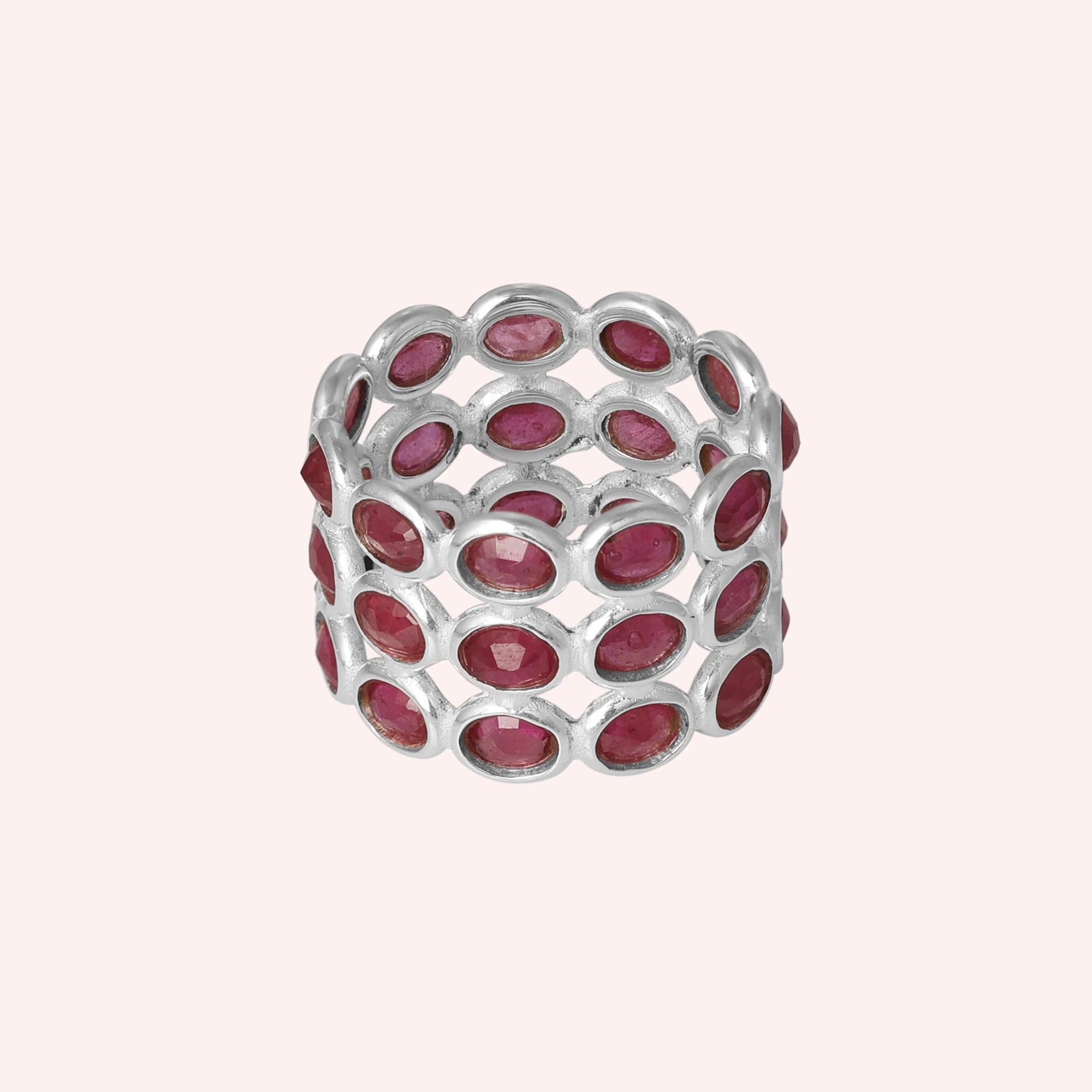 Wide silver ruby eternity ring band featuring oval-cut rubies in an open setting on a pink background from a direct front angle.