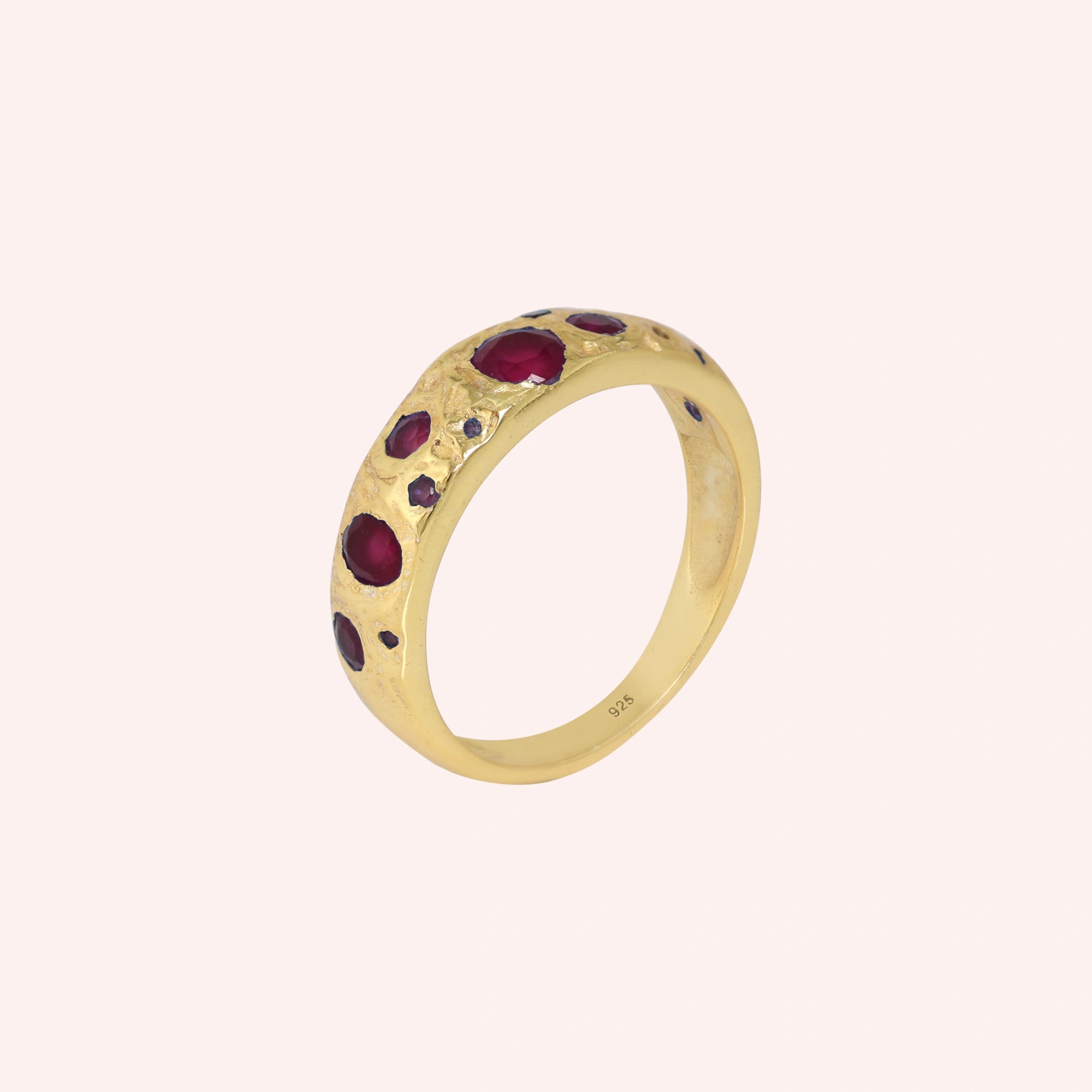 Ruby_stone_ring_in_gold_plated_silver_with_multiple_ruby_stones_at_slight_angle_on_solid_pink_background