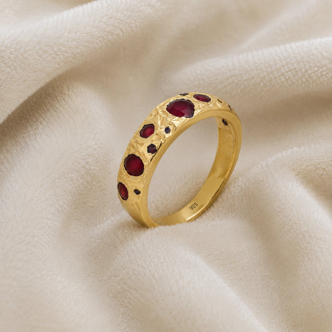Ruby_stone_ring_in_gold_plated_silver_with_multiple_ruby_stones_at_slight_angle_on_soft_fabric_background