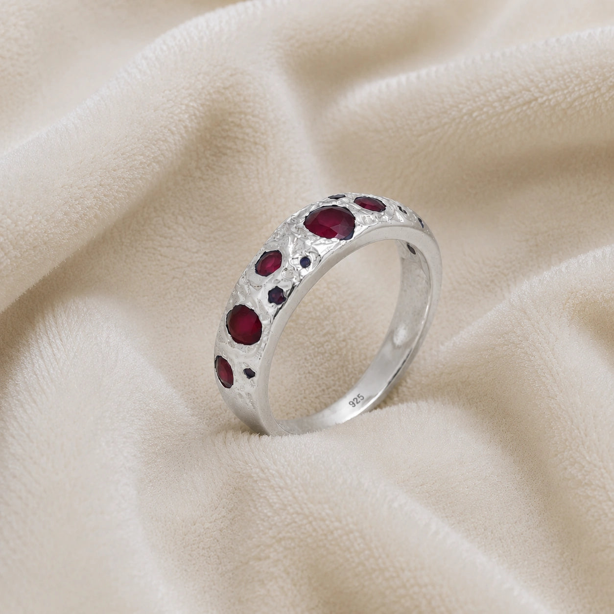 Ruby_stone_ring_in_sterling_silver_with_multiple_ruby_stones_at_slight_angle_on_soft_fabric_background