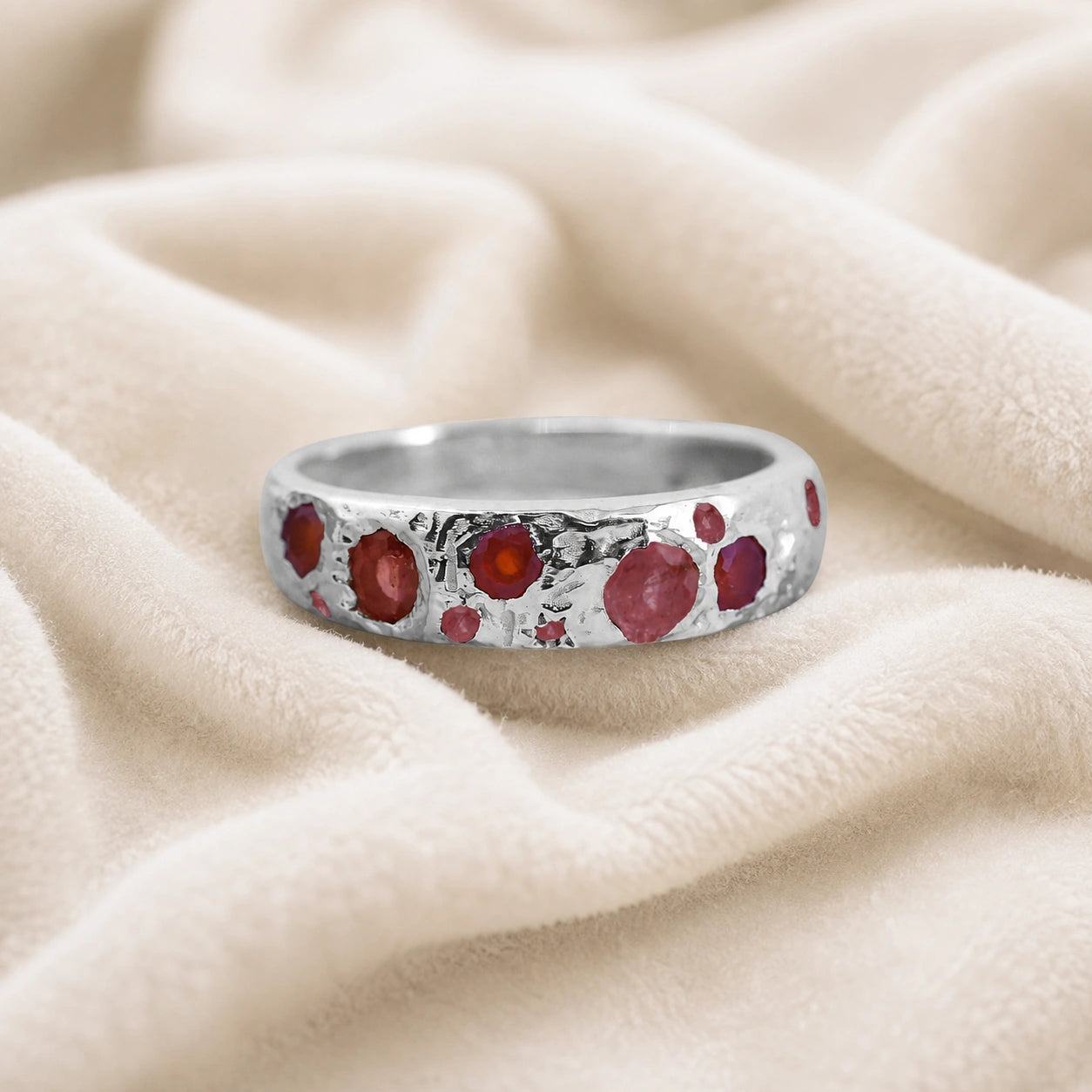Ruby_stone_ring_in_sterling_silver_with_multiple_ruby_stones_at_front_angle_on_soft_fabric_background