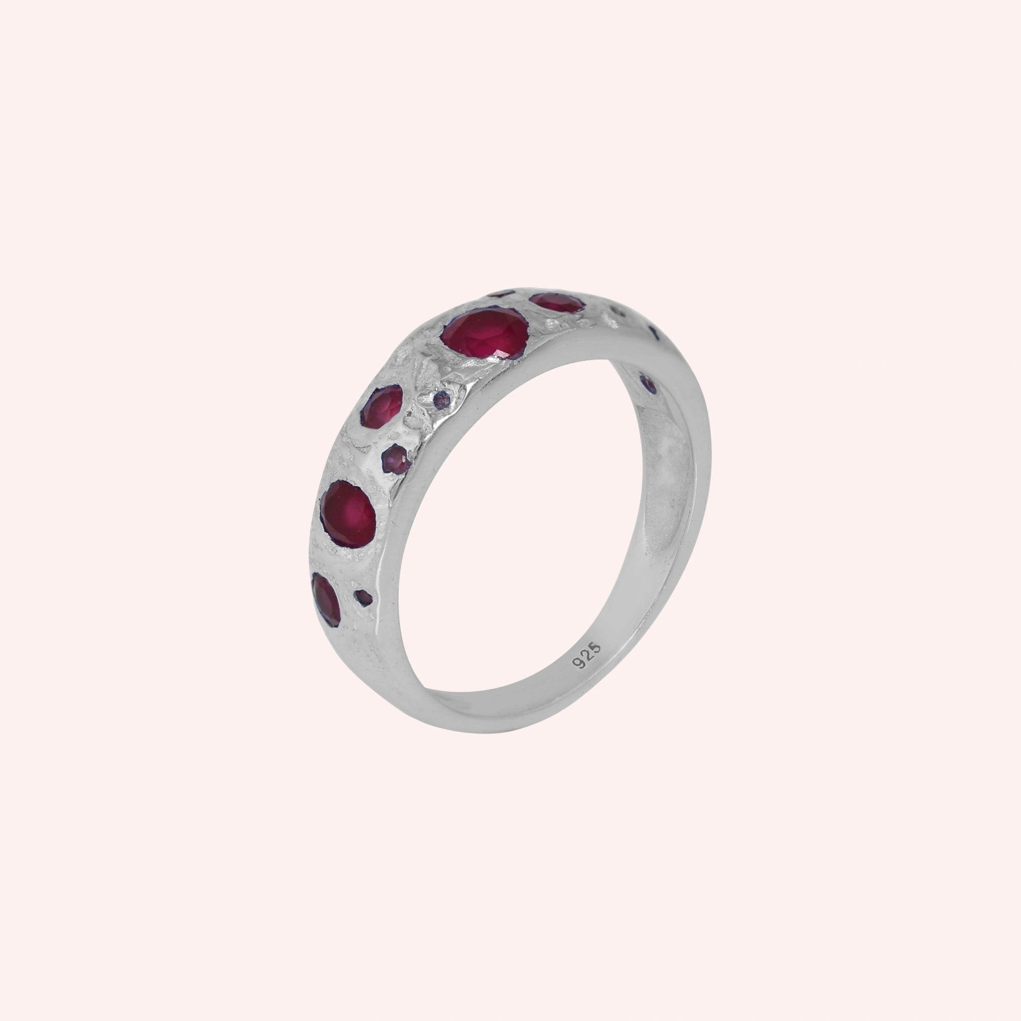 Ruby_stone_ring_in_sterling_silver_with_multiple_ruby_stones_at_slight_angle_on_solid_pink_background