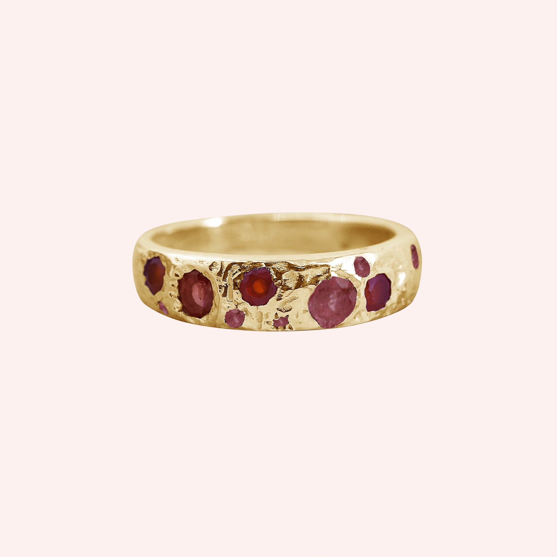 Ruby_stone_ring_in_gold_plated_silver_with_multiple_ruby_stones_at_front_angle_on_solid_pink_background