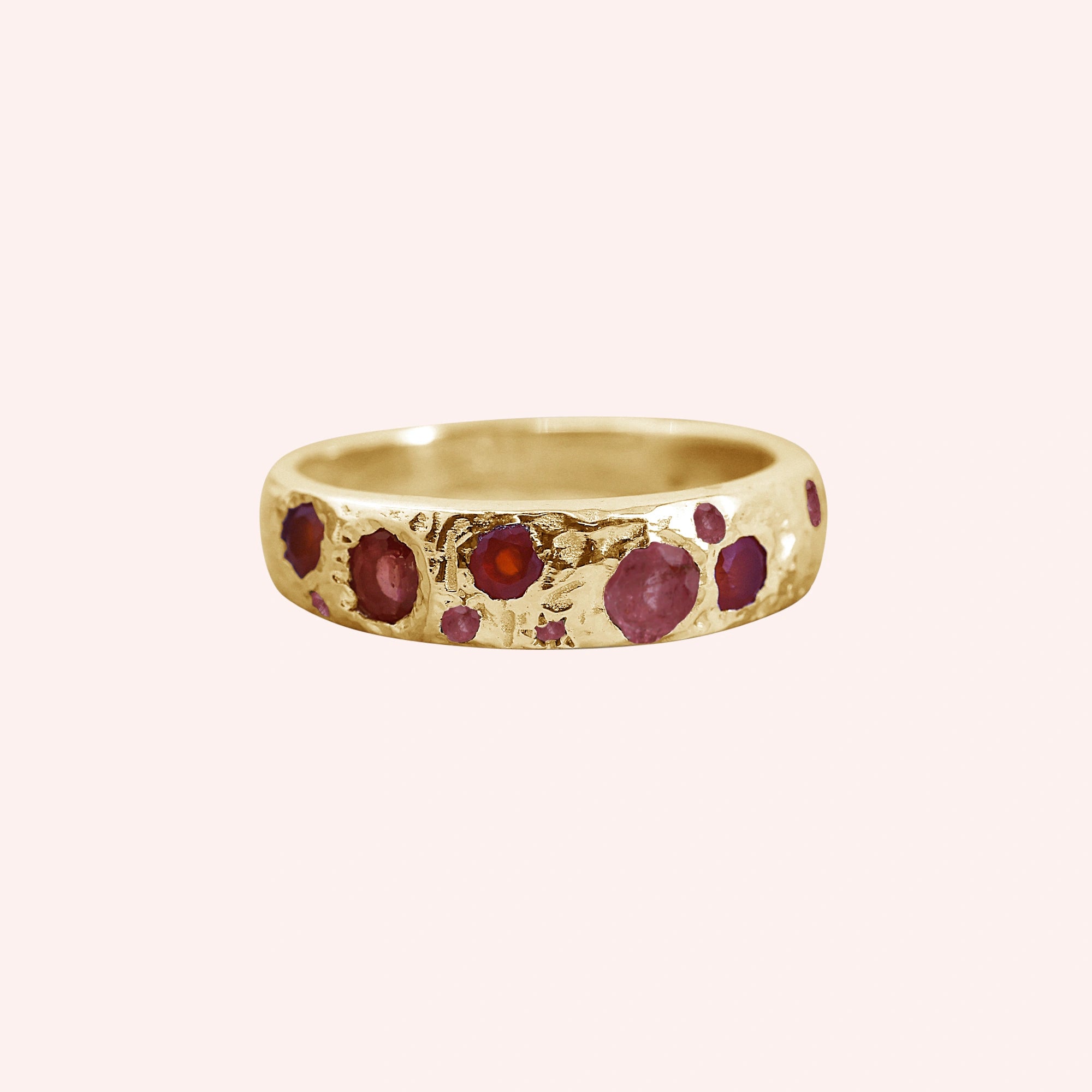 Ruby_stone_ring_in_gold_plated_silver_with_multiple_ruby_stones_at_front_angle_on_solid_pink_background