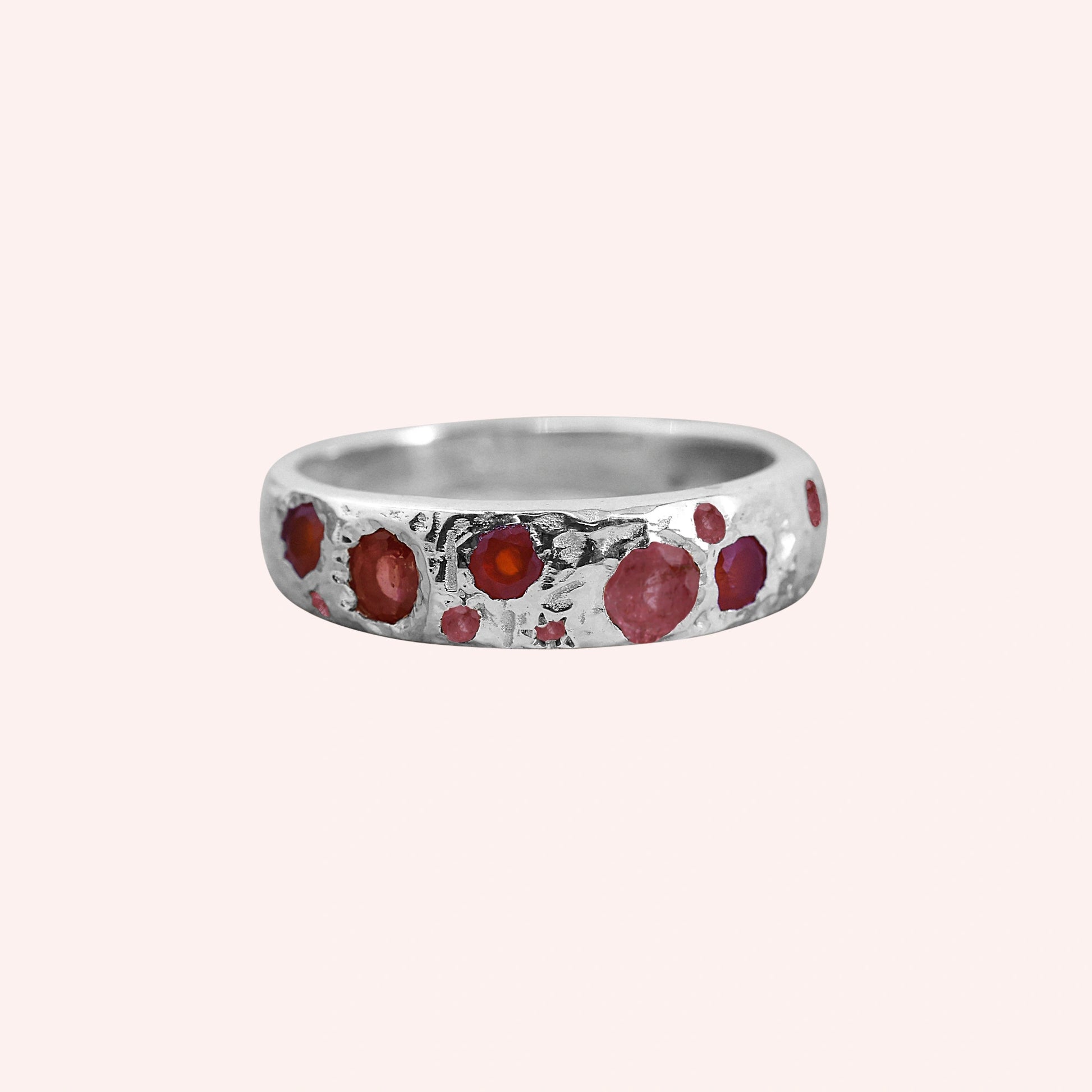 Ruby_stone_ring_in_sterling_silver_with_multiple_ruby_stones_at_front_angle_on_solid_pink_background