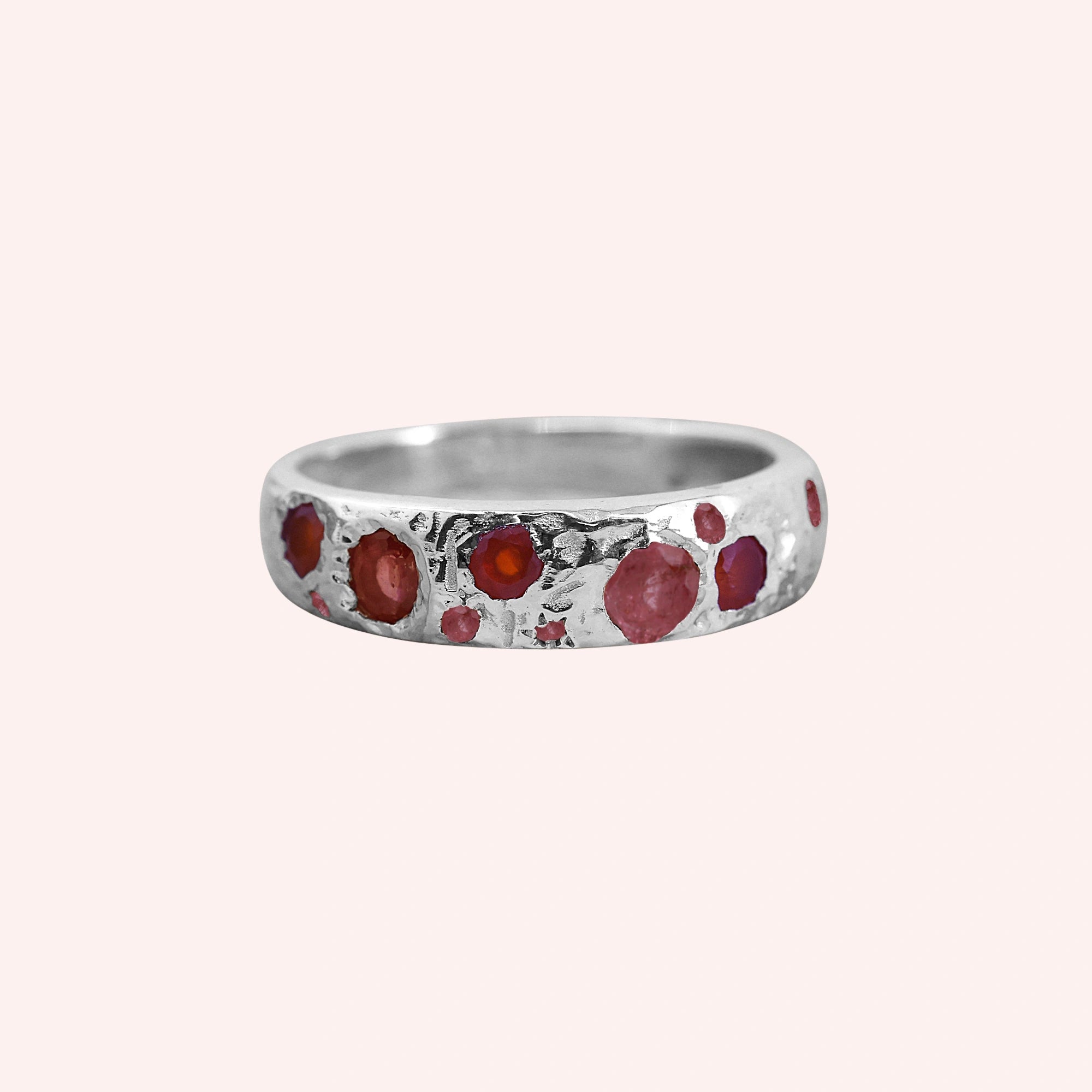 Ruby_stone_ring_in_sterling_silver_with_multiple_ruby_stones_at_front_angle_on_solid_pink_background
