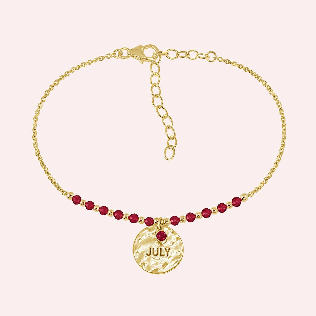 Birthstone_bracelet_in_gold_plated_silver_with_July_charm_and_ruby_beads_on_fine_chain_on_solid_pink_background
