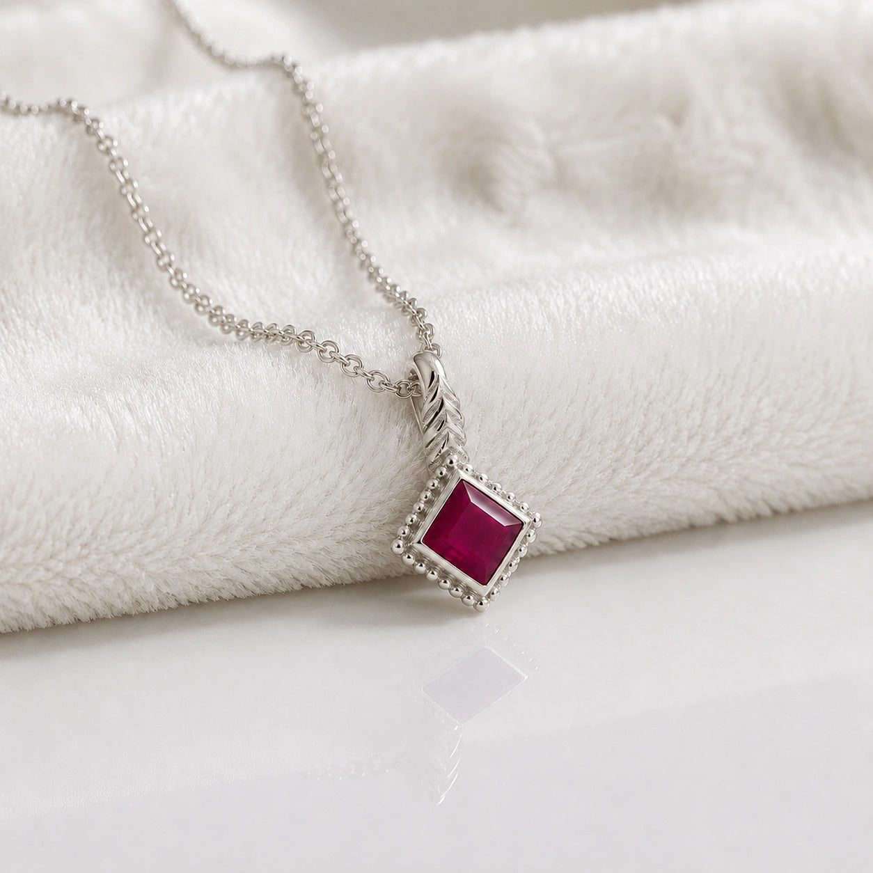 Birthstone_necklace_in_sterling_silver_with_square_cut_ruby_pendant_in_slighlty_angled_view_on_soft_white_fabric_background