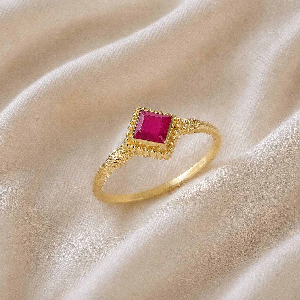 Princess_cut_ring_gold_plated_silver_with_square_ruby_and_detailed_band_slightly_tilted_view_on_soft_fabric_background