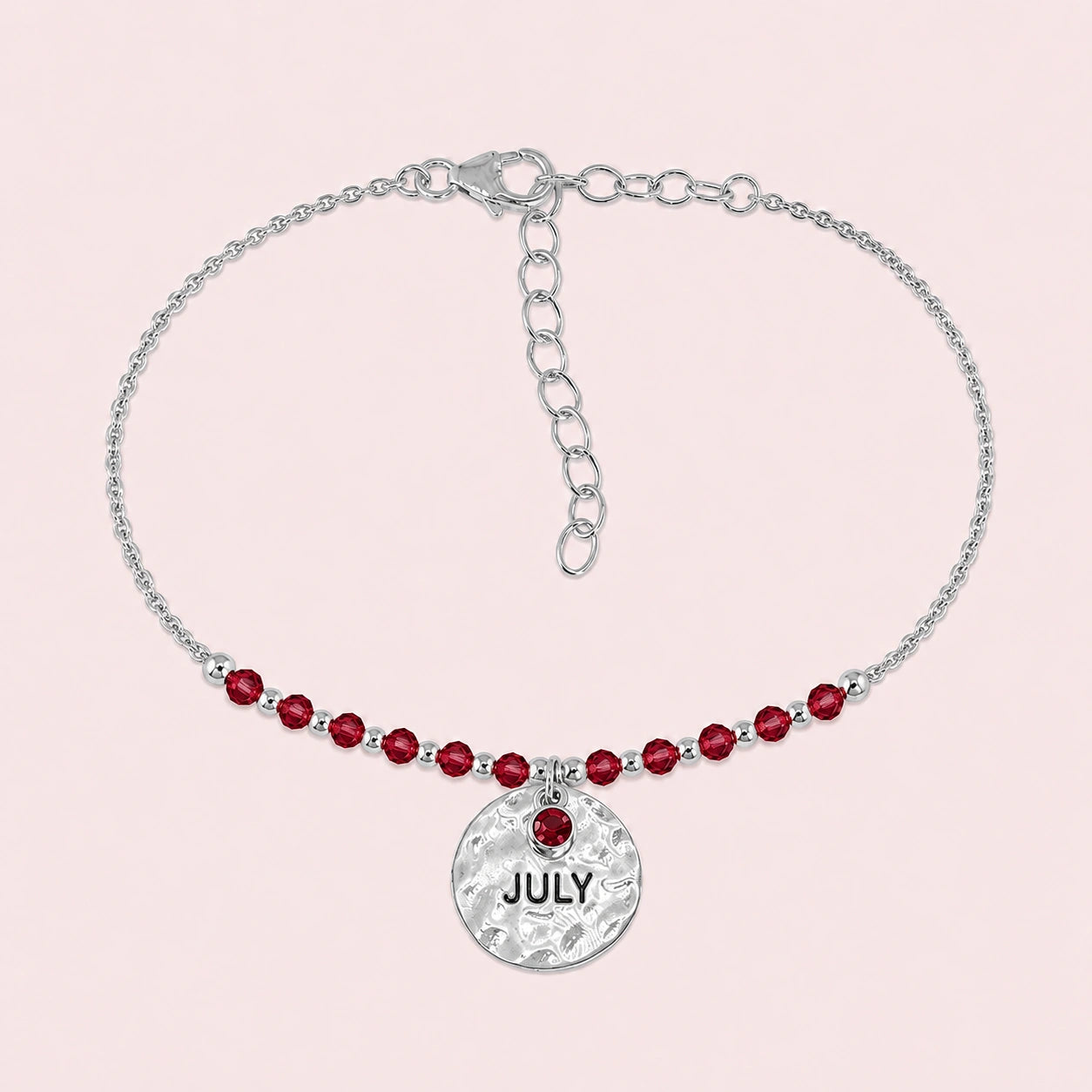 Birthstone_bracelet_in_sterling_silver_with_July_charm_and_ruby_beads_on_fine_chain_on_solid_pink_background