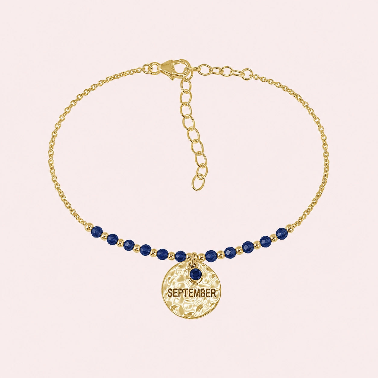 Birthstone_bracelet_in_gold_plated_silver_with_September_charm_and_sapphire_beads_on_fine_chain_on_solid_pink_background