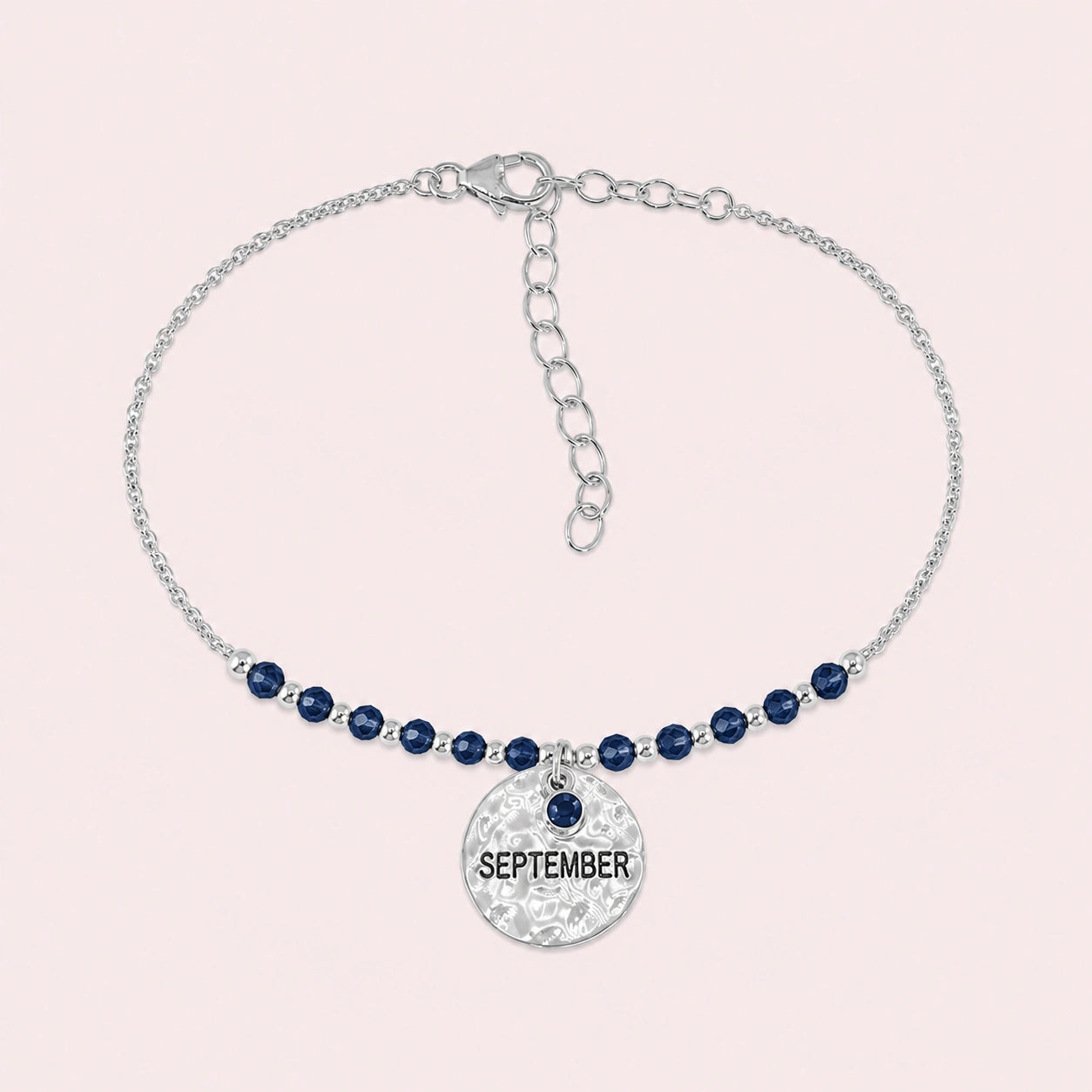 Birthstone_bracelet_in_sterling_silver_with_September_charm_and_sapphire_beads_on_fine_chain_on_solid_pink_background