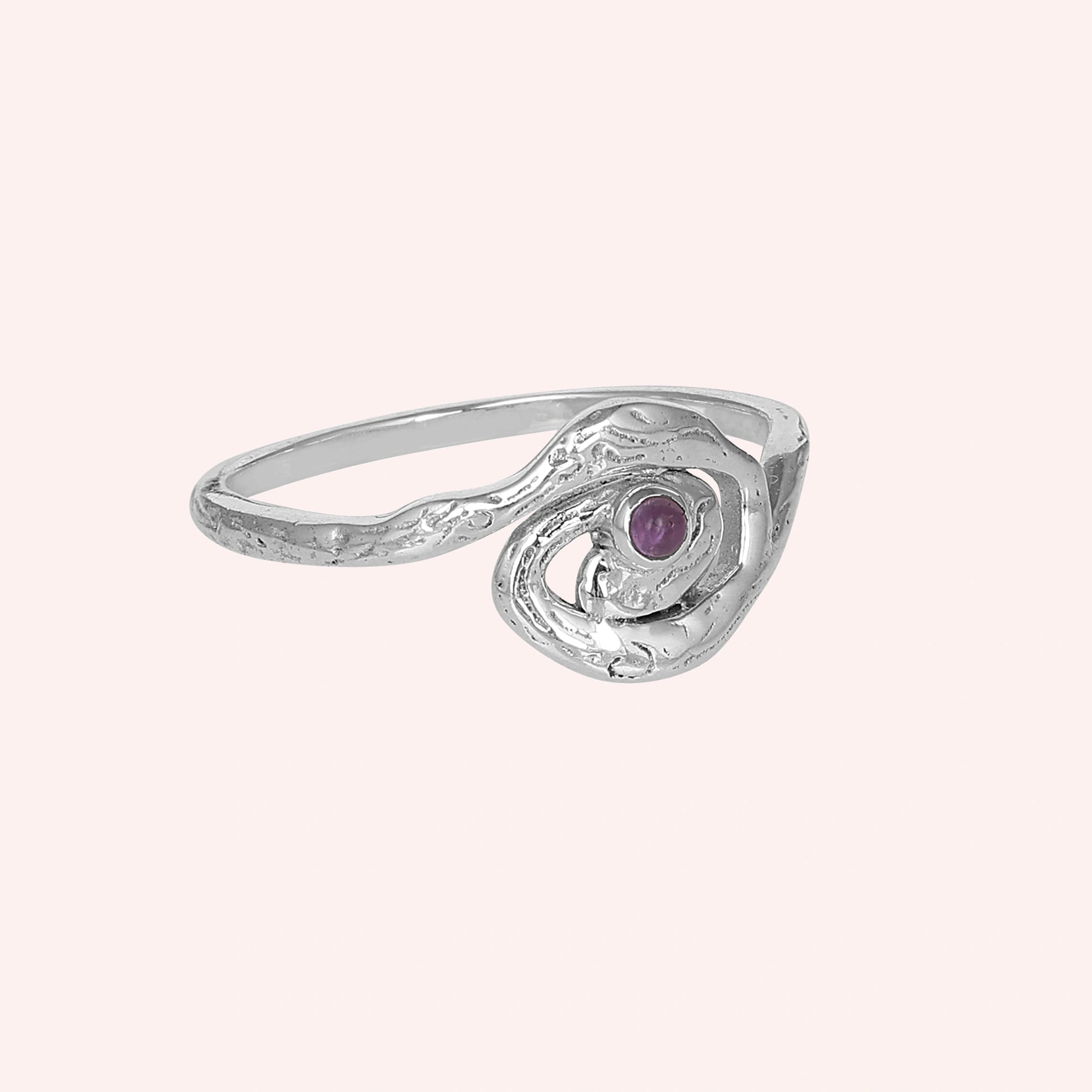 A silver amethyst ring with a swirl design shown from a side angle over a light pink background celestial jewelry inspired