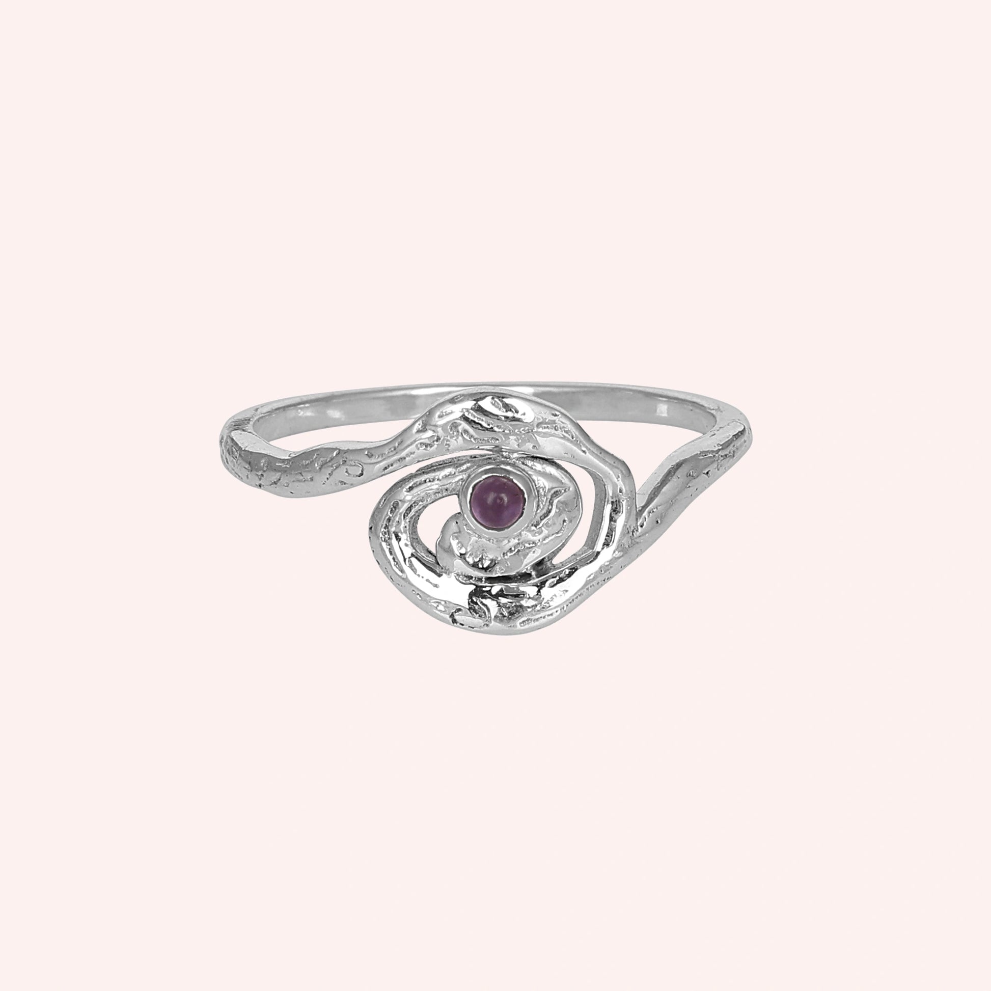 A front angle view of a silver amethyst ring with celestial jewelry swirl designs on a plain light pink solid color background