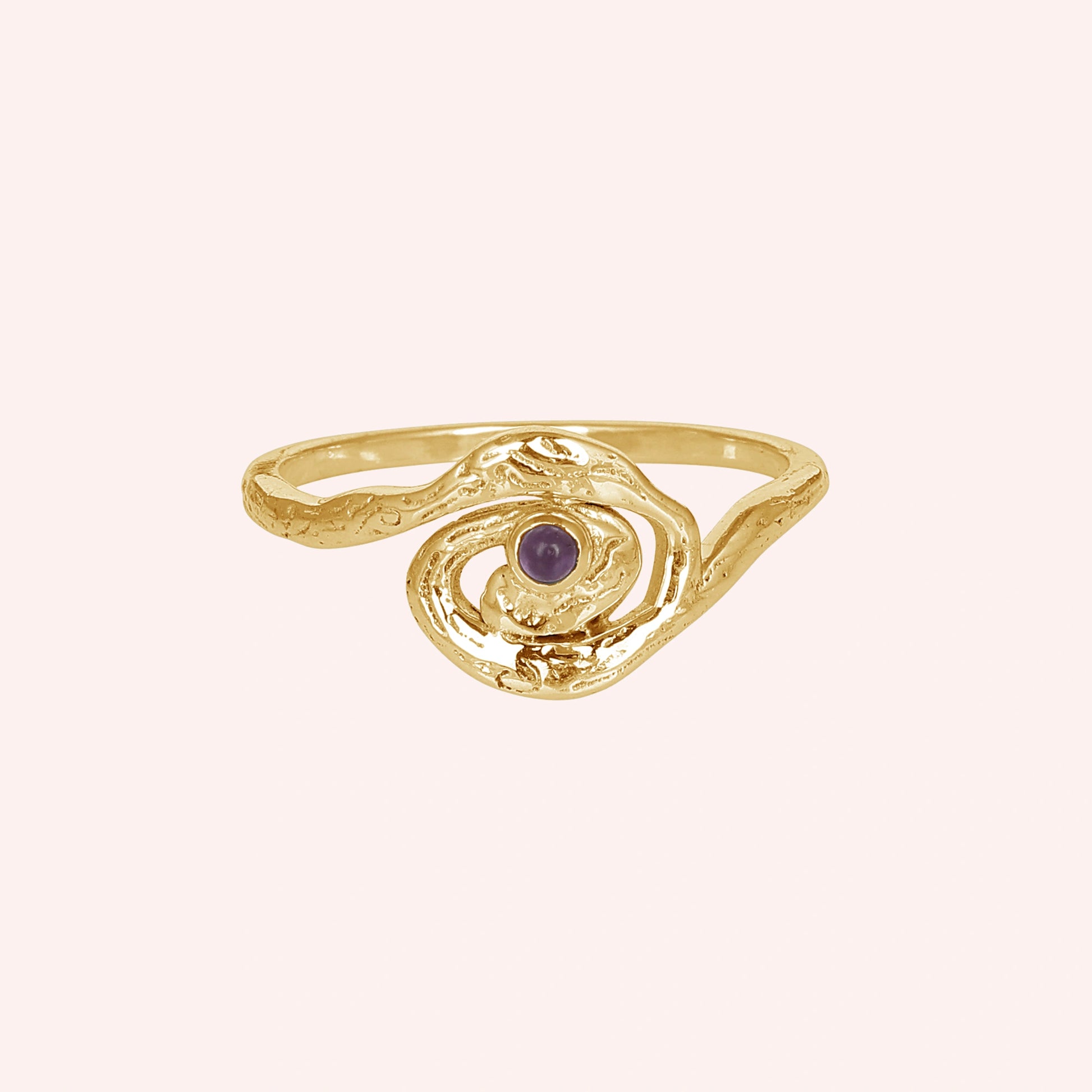 A gold plated silver amethyst ring with a galaxy swirl design at a front angle on a pale pink background celestial jewelry