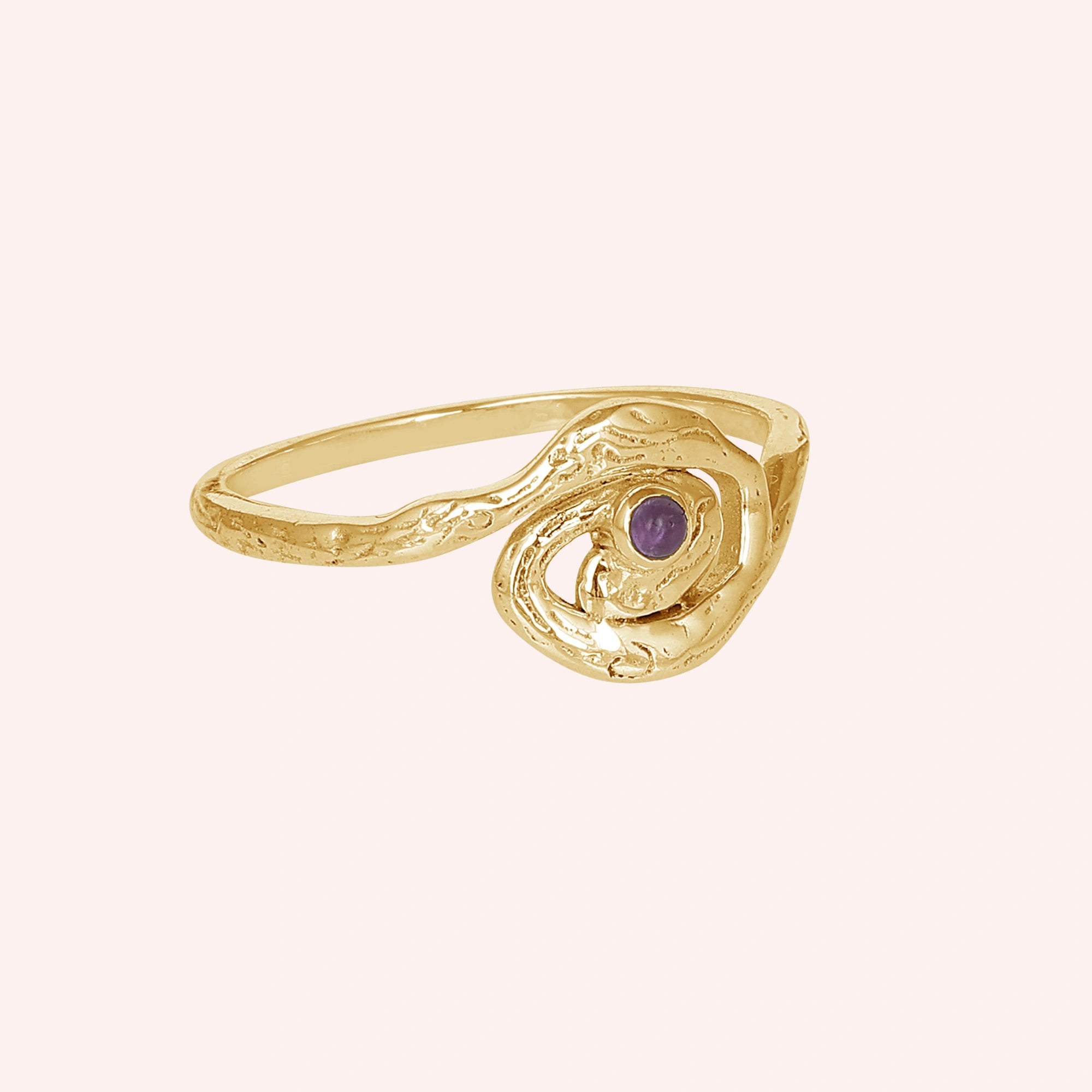 A gold plated silver amethyst ring with a galaxy swirl design at a side angle on a pale pink background celestial jewelry
