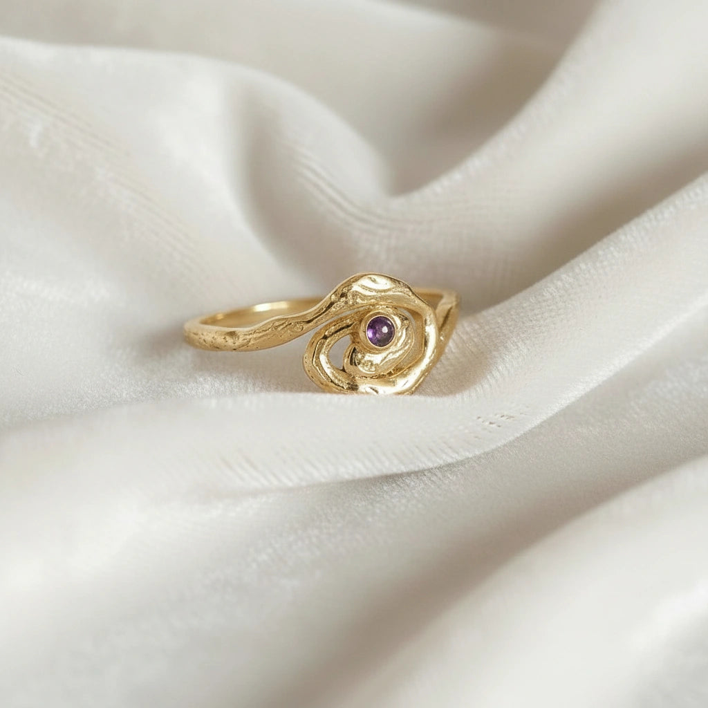 A gold plated silver amethyst ring with a galaxy swirl design at a side angle on an off white fabric background celestial jewelry