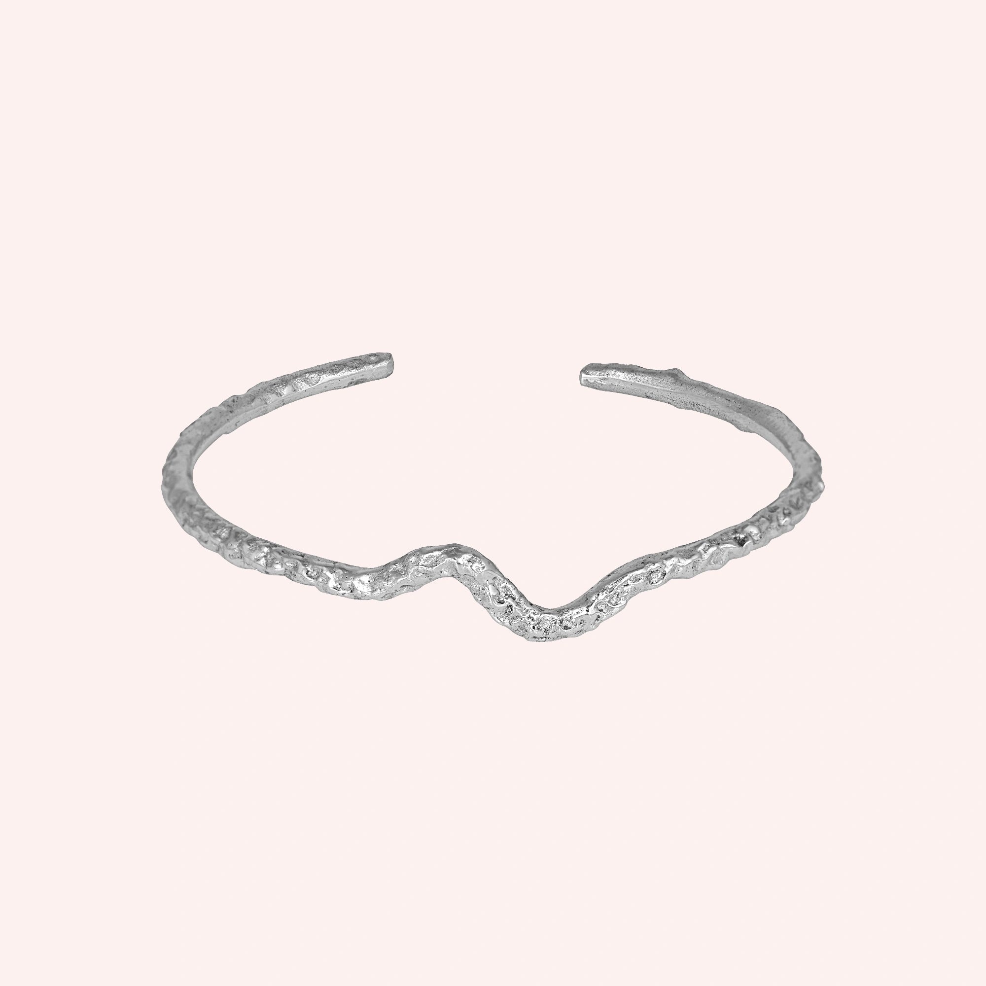 Silver cuff bracelet shown at front angled view featuring textured open silver cuff design on a soft pink background