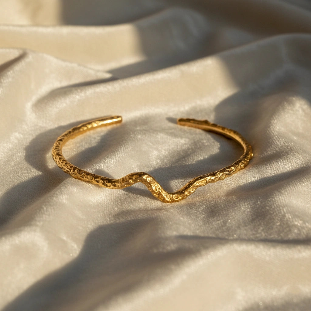 Silver cuff bracelet shown at front angled view featuring gold plated textured open cuff resting on soft cream fabric background