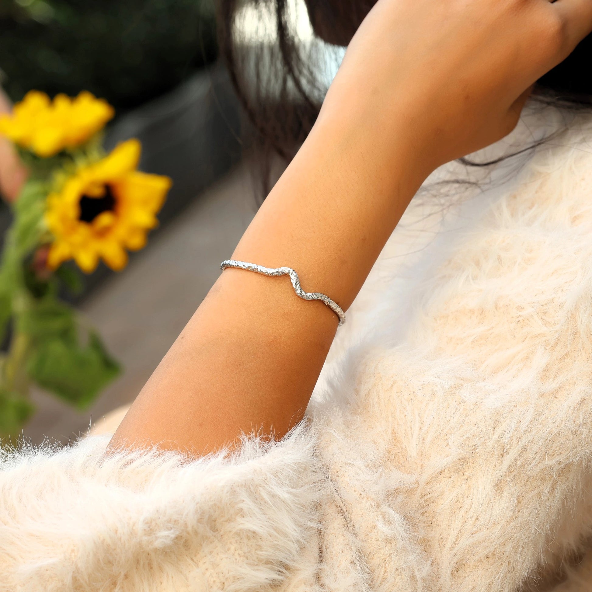 Silver cuff bracelet shown at side angled view worn on wrist featuring textured wave design with soft fur sleeve background