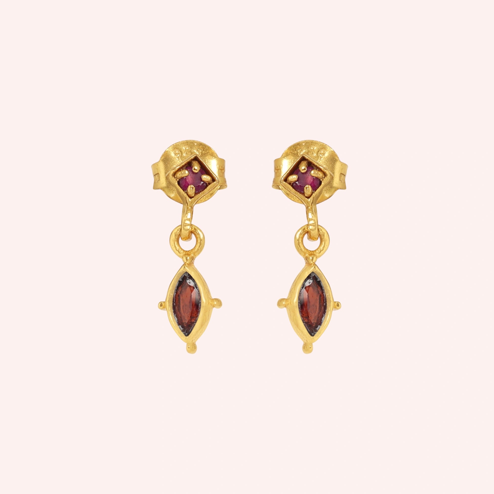 Silver_drop_earrings_in_gold_plated_silver_with_ruby_and_garnet_stones_at_front_angle_view_on_solid_pink_background