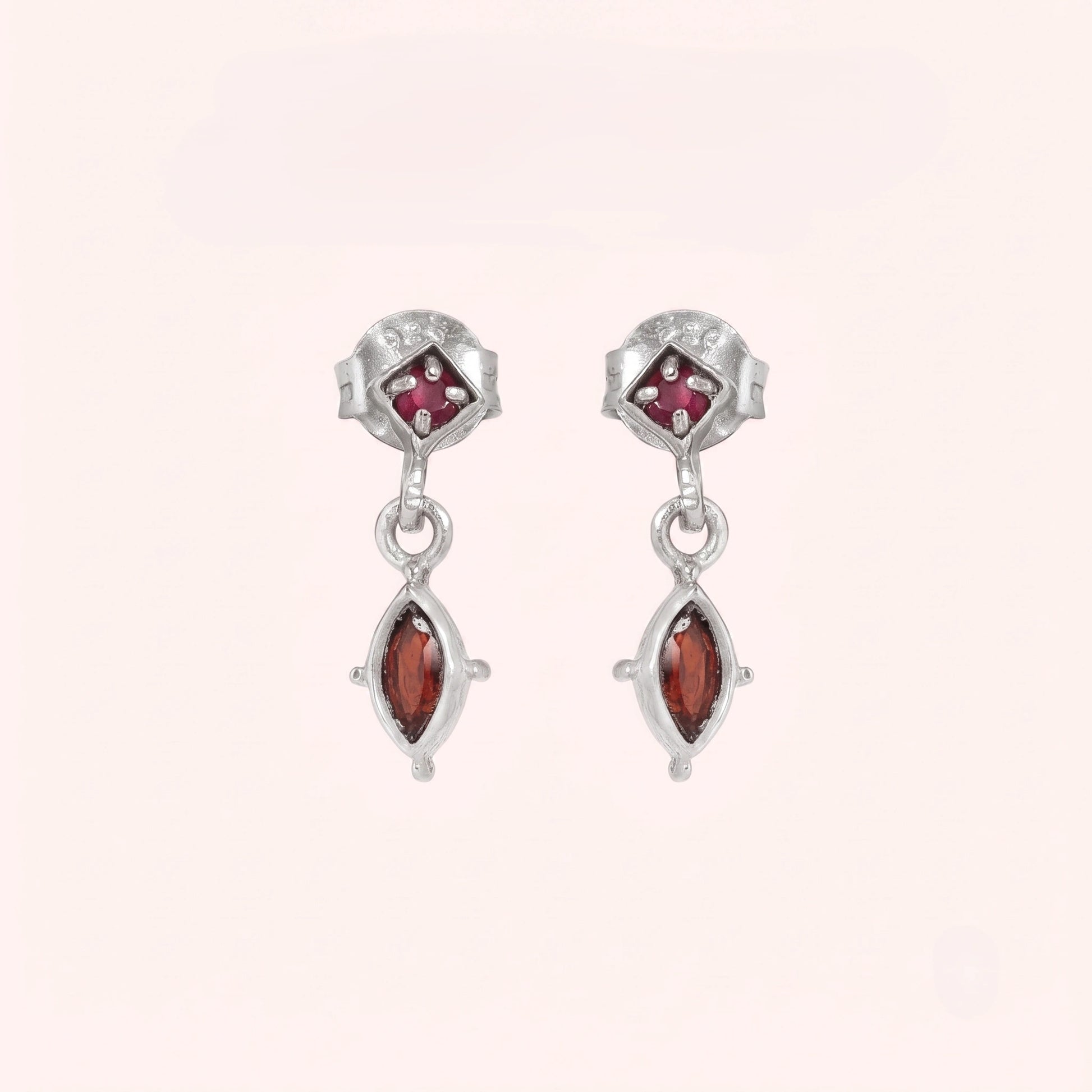 Silver_drop_earrings_in_sterling_silver_with_ruby_and_garnet_stones_at_front_angle_view_on_solid_pink_background