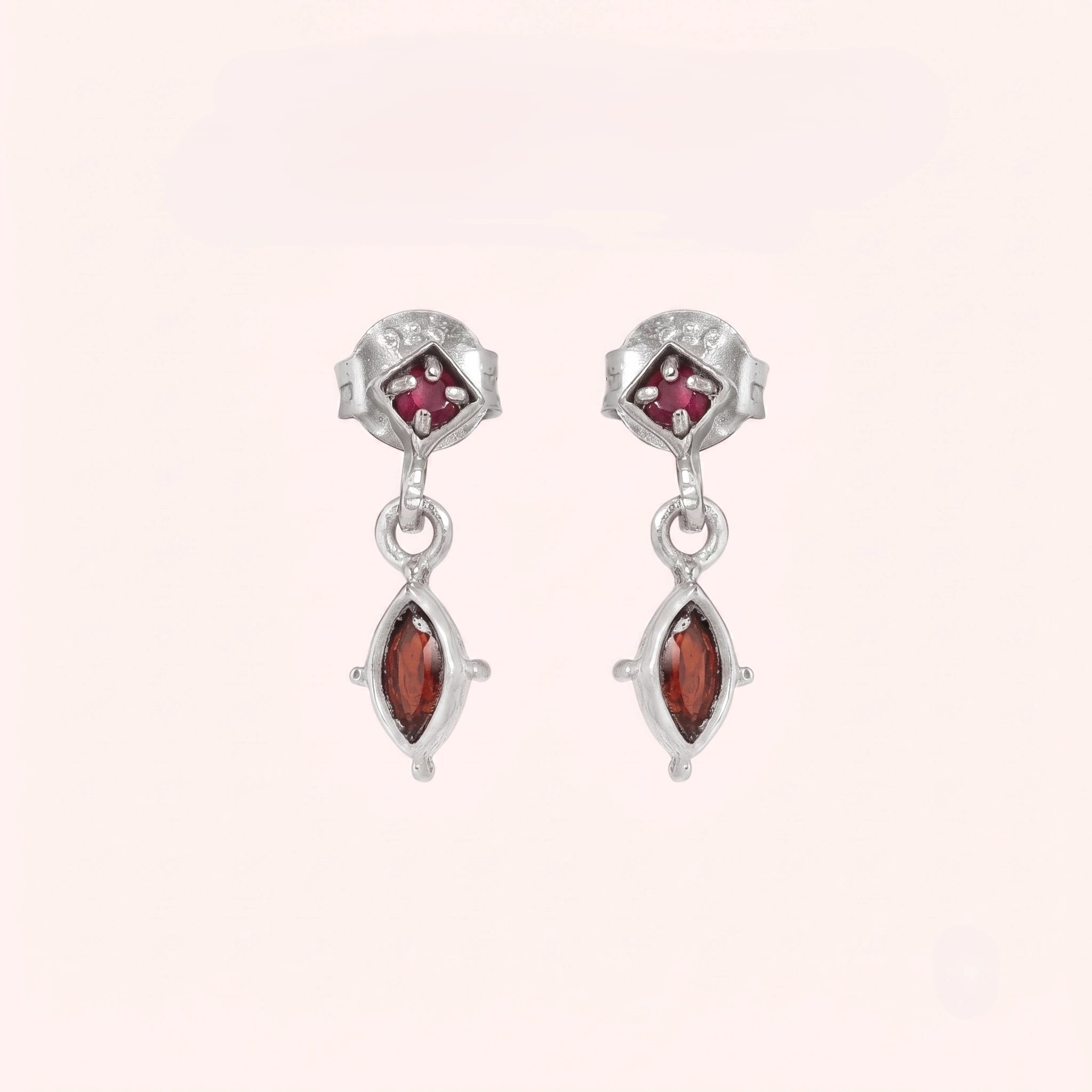Silver_drop_earrings_in_sterling_silver_with_ruby_and_garnet_stones_at_front_angle_view_on_solid_pink_background
