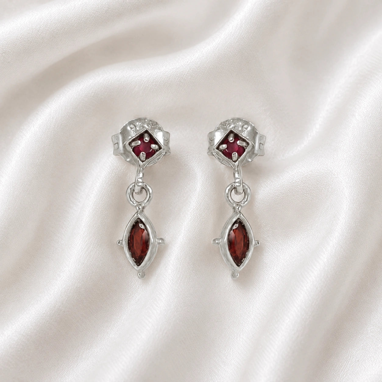 Silver_drop_earrings_in_sterling_silver_with_ruby_and_garnet_stones_at_front_angle_view_on_soft_fabric_background