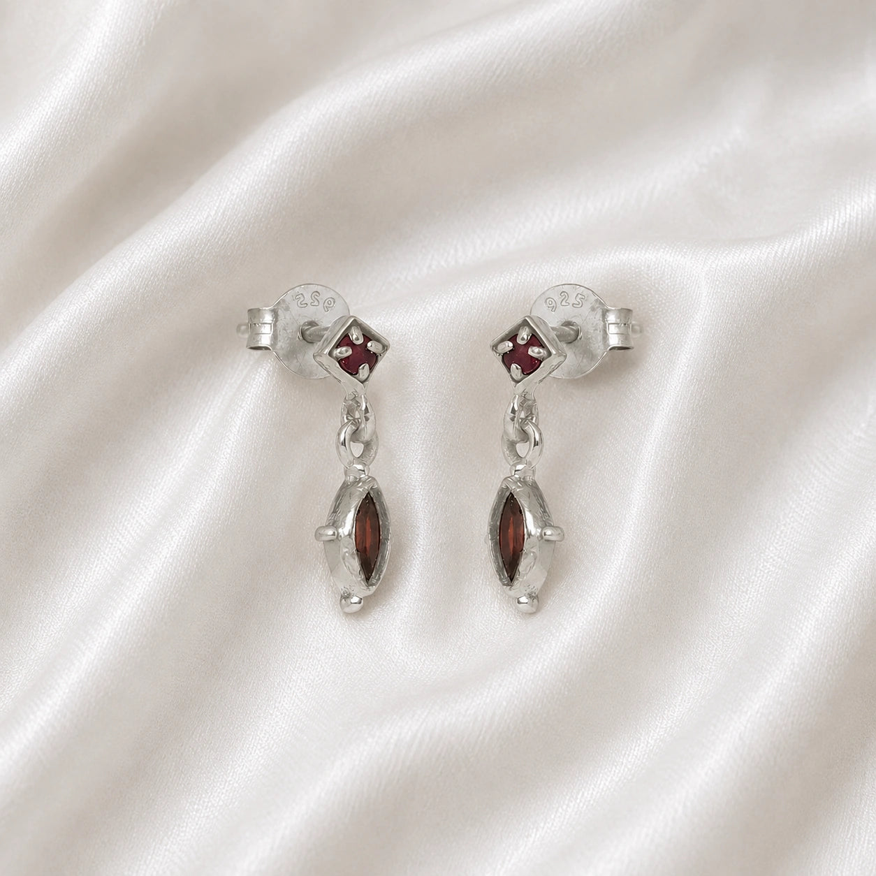 Silver_drop_earrings_in_sterling_silver_with_ruby_and_garnet_stones_at_slight_angle_view_on_soft_fabric_background