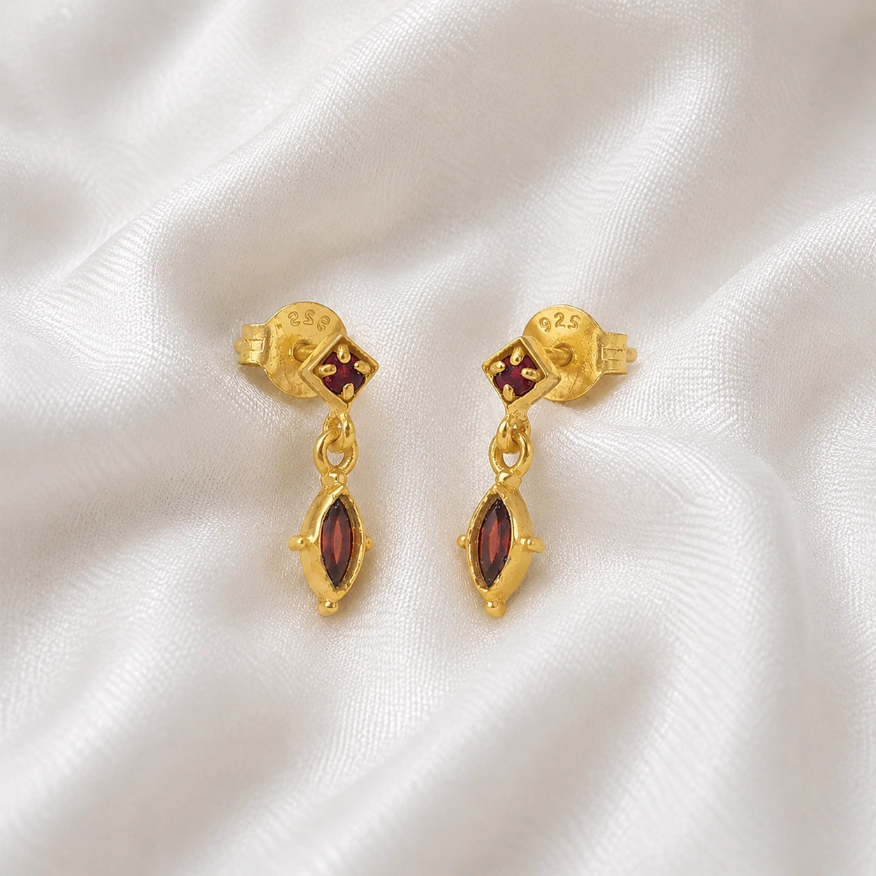 Silver_drop_earrings_in_gold_plated_silver_with_ruby_and_garnet_stones_at_slight_angle_view_on_soft_fabric_background