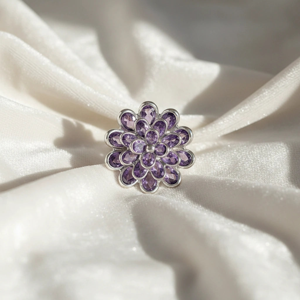 silver_flower_ring_flower_engagement_ring_with_purple_gem_petals_in_silver_setting_top_view_on_soft_white_fabric_background