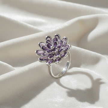 silver_flower_ring_flower_engagement_ring_with_purple_gem_petals_in_silver_setting_angled_view_on_soft_white_fabric_background