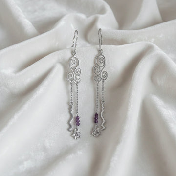 front_angle_silver_hanging_earrings_with_scroll_links_and_purple_beads_trendy_earrings_on_soft_white_fabric_background