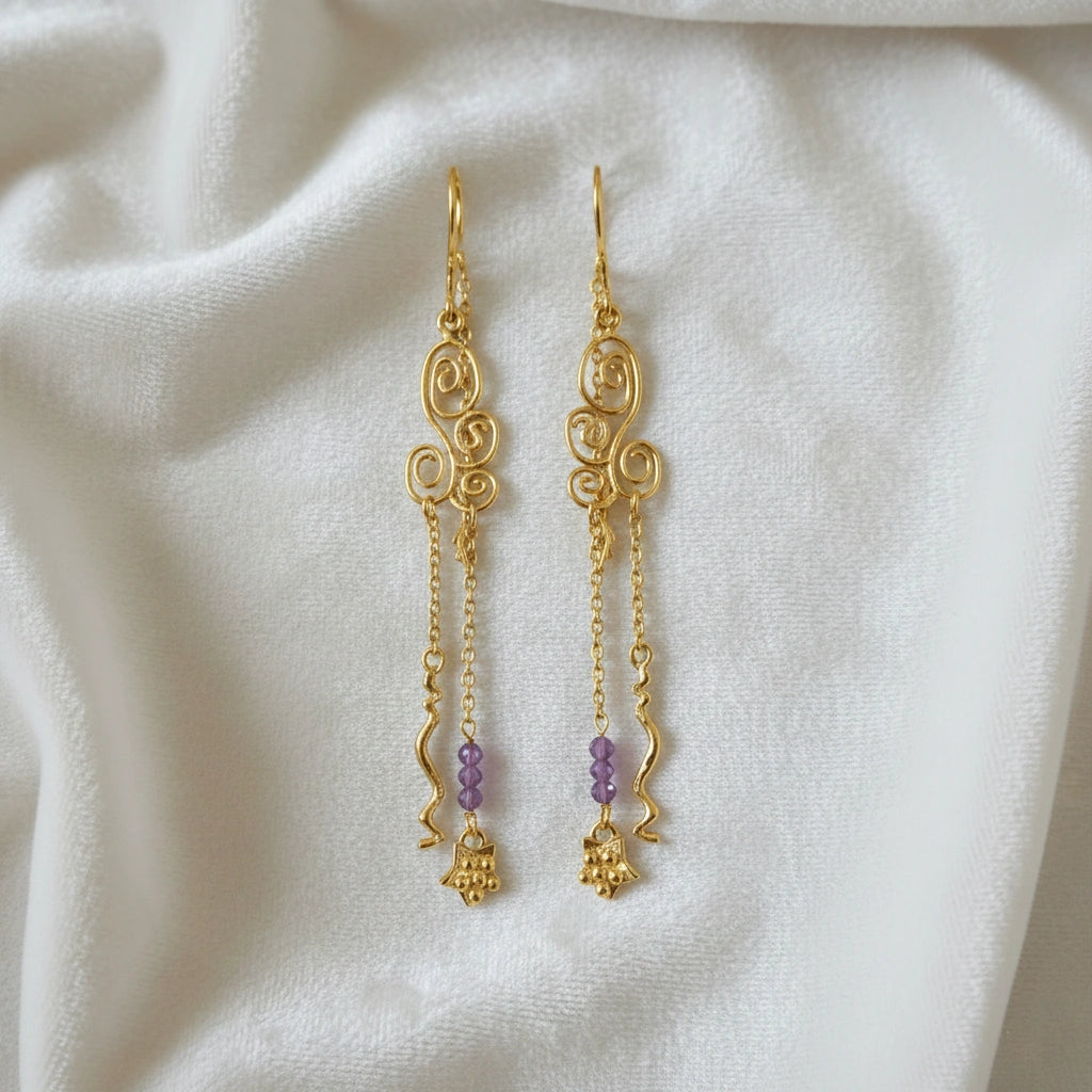 front_angle_silver_hanging_earrings_gold_plated_scroll_design_with_purple_beads_and_chain_details_trendy_earrings_on_fabric
