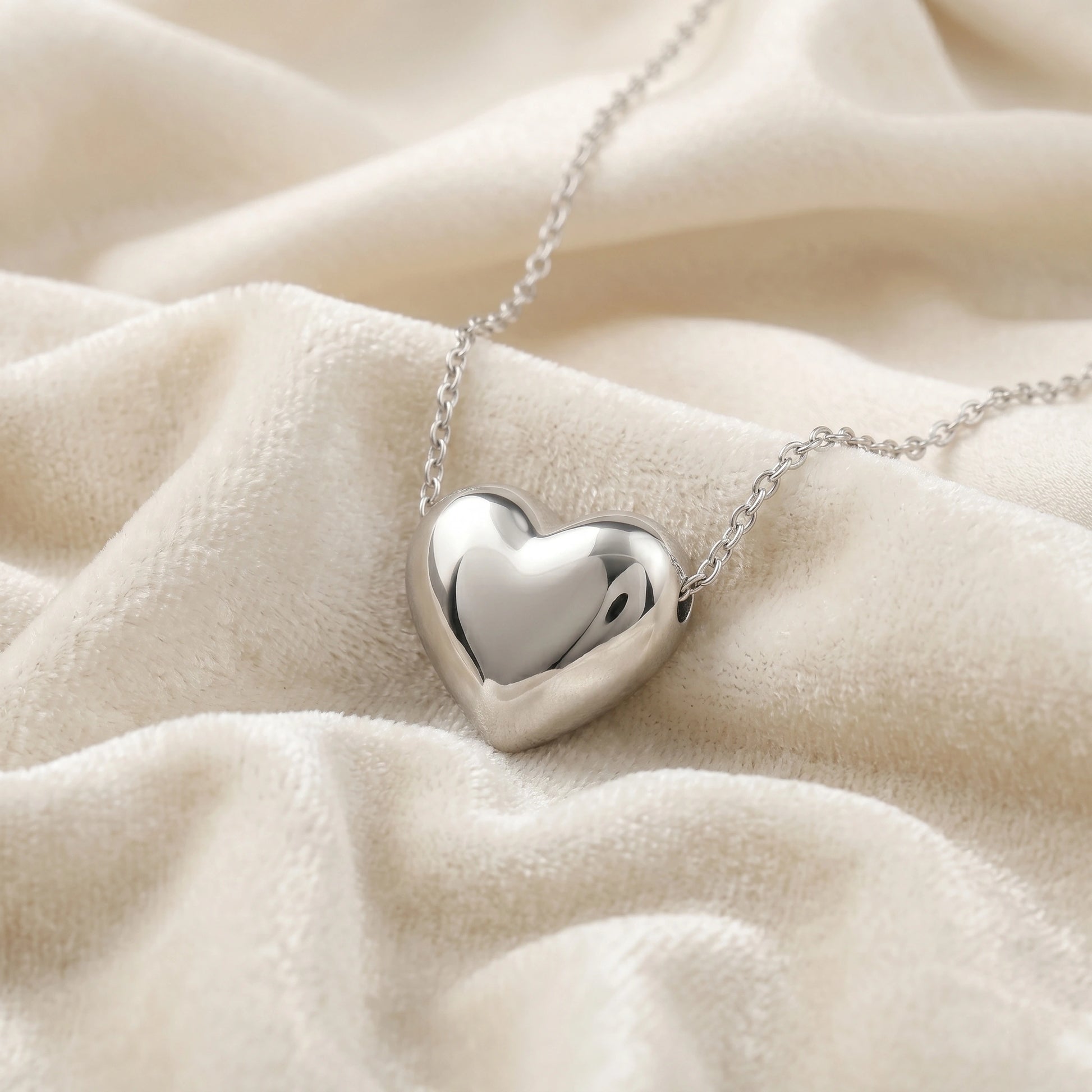 Silver_heart_necklace_shown_in_slightly_angled_view_with_sterling_silver_with_chain_on_soft_white_fabric_background