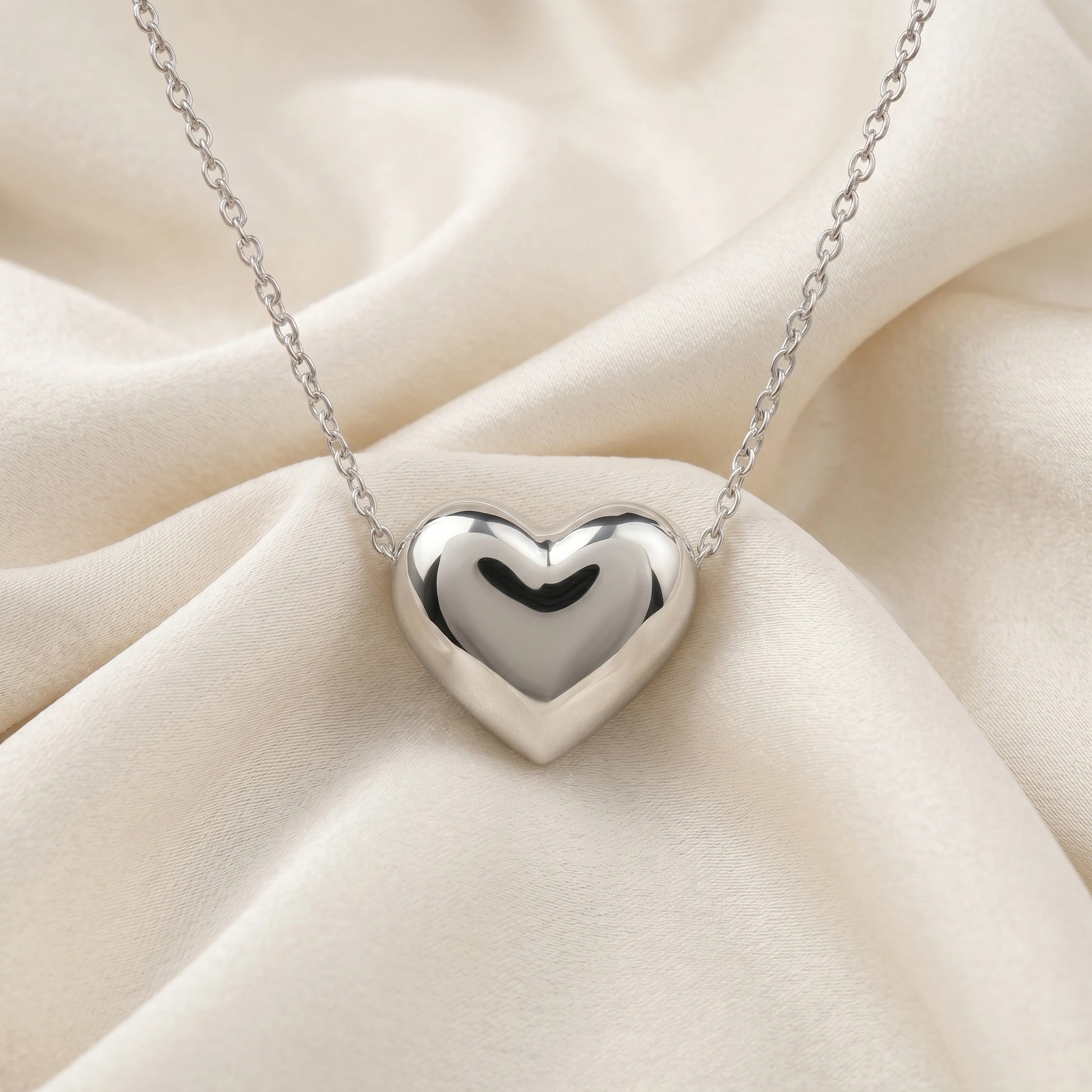 Silver_heart_necklace_shown_in_front_angled_view_with_sterling_silver_with_chain_on_soft_fabric_background