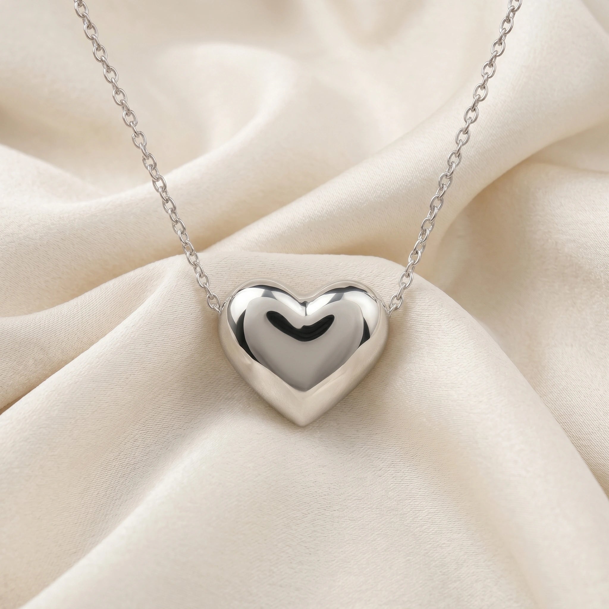 Silver_heart_necklace_shown_in_front_angled_view_with_sterling_silver_with_chain_on_soft_fabric_background