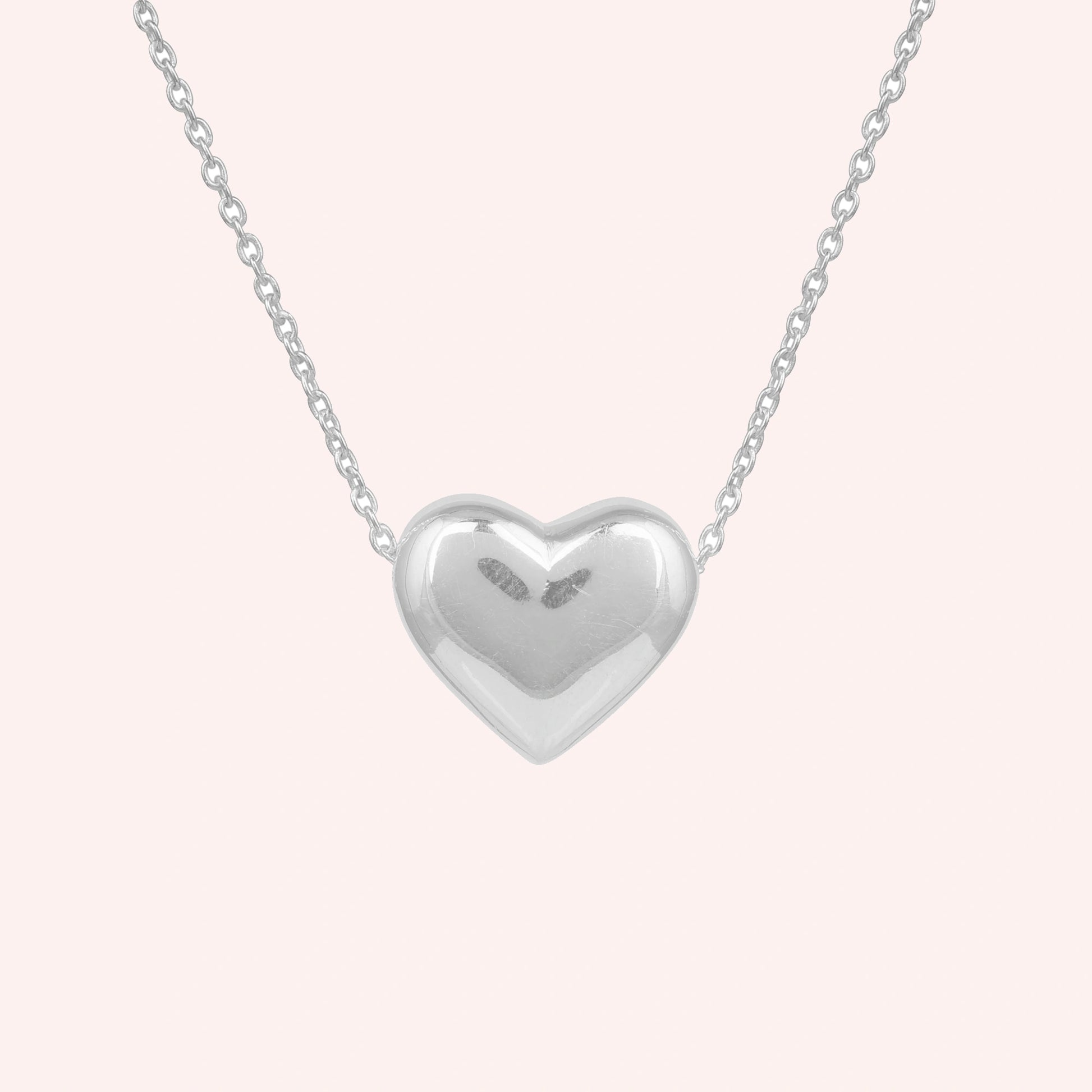 Silver_heart_necklace_shown_in_front_angled_view_with_sterling_silver_with_chain_on_solid_pink_background