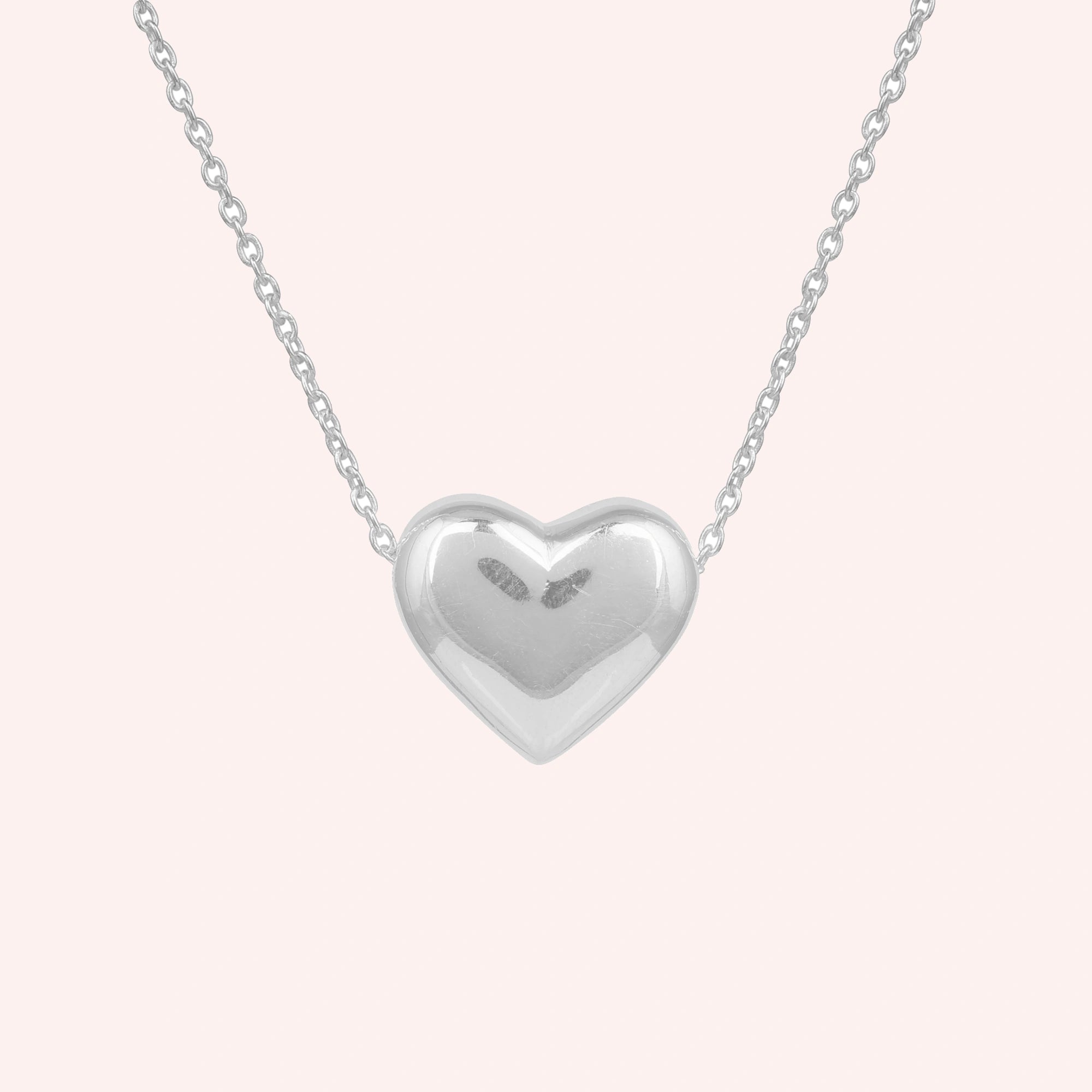 Silver_heart_necklace_shown_in_front_angled_view_with_sterling_silver_with_chain_on_solid_pink_background