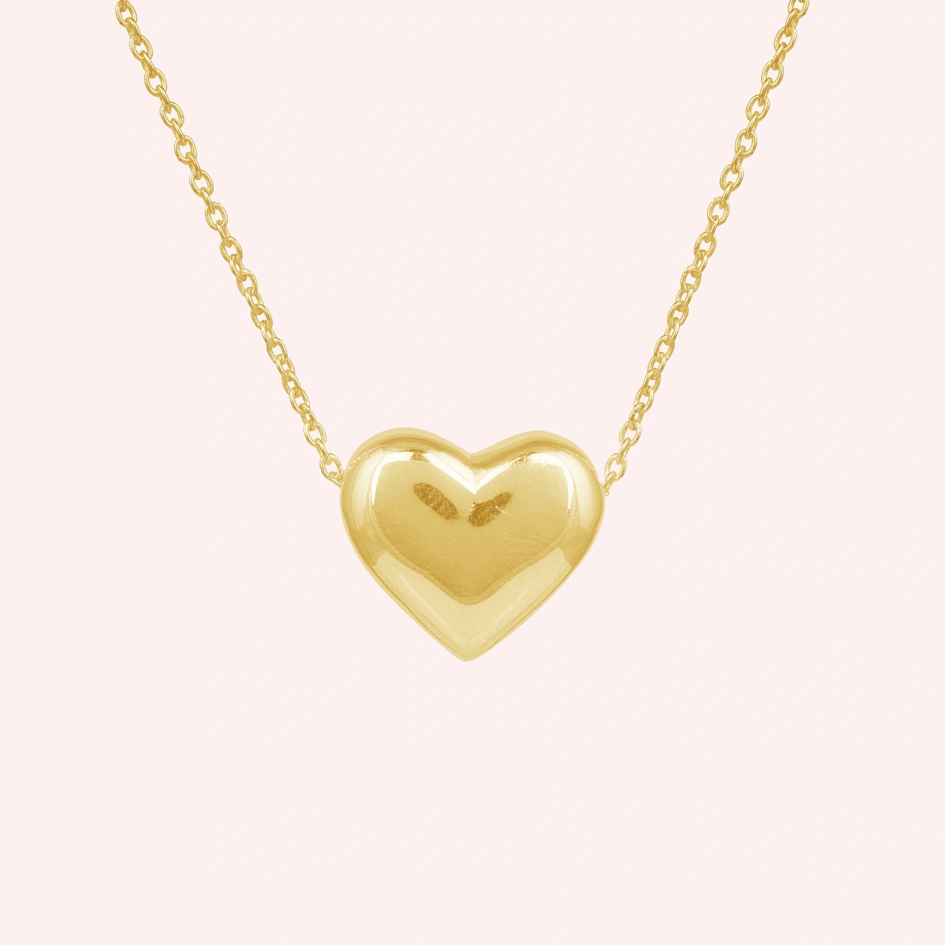 Silver_heart_necklace_shown_in_front_angled_view_with_gold_plated_silver_with_chain_on_solid_pink_background