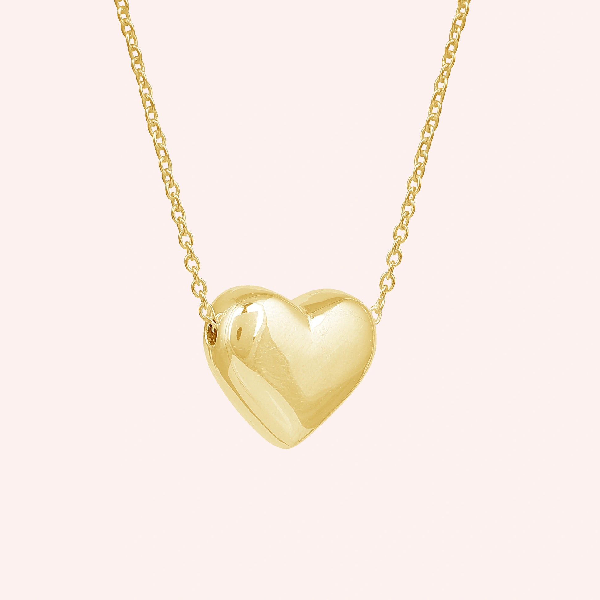 Silver_heart_necklace_shown_in_slightly_angled_view_with_gold_plated_silver_with_chain_on_solid_pink_background