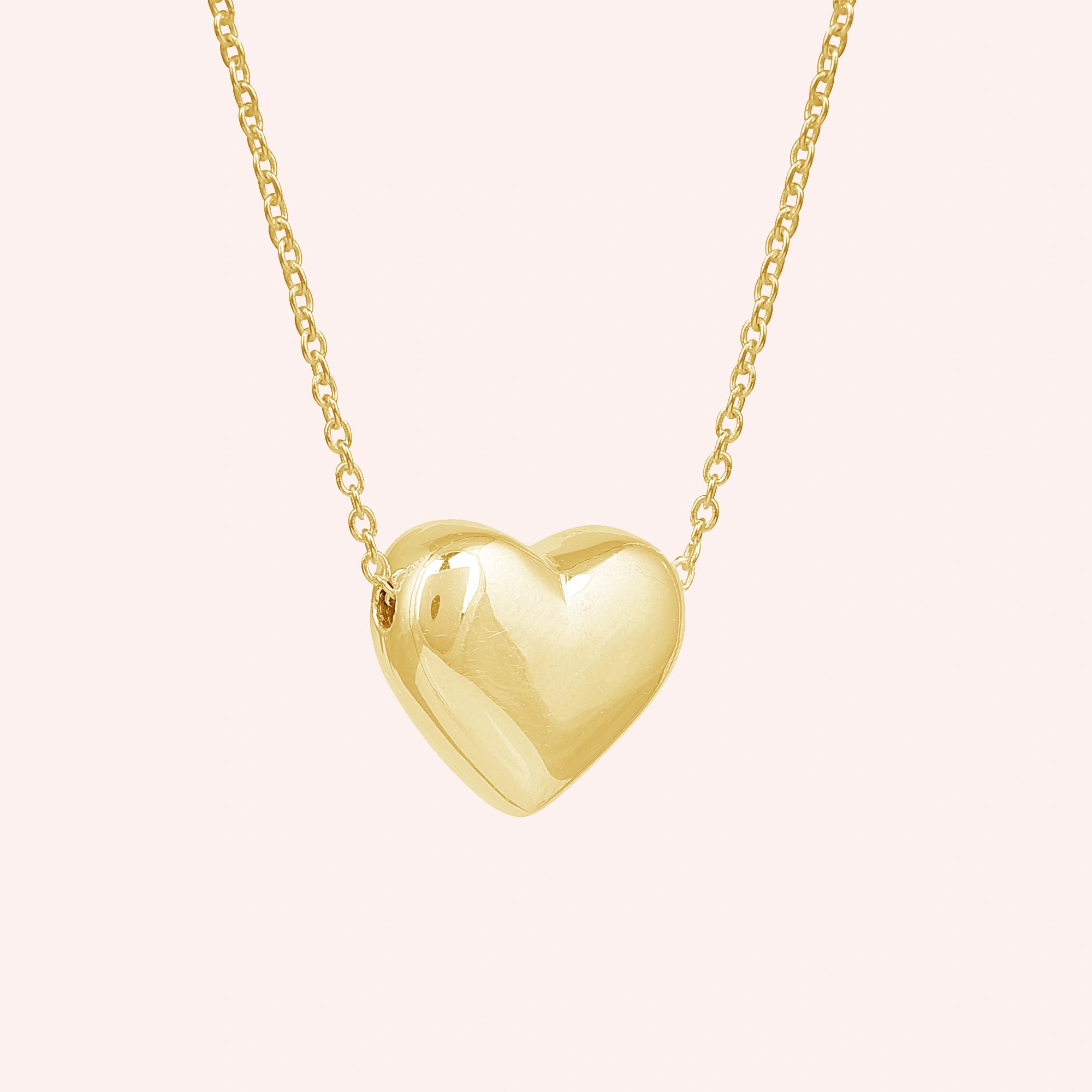 Silver_heart_necklace_shown_in_slightly_angled_view_with_gold_plated_silver_with_chain_on_solid_pink_background