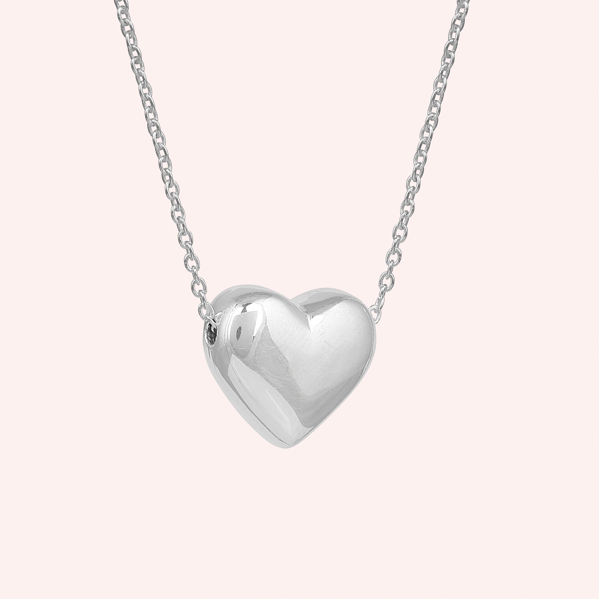 Silver_heart_necklace_shown_in_slightly_angled_view_with_slightly_silver_with_chain_on_solid_pink_background