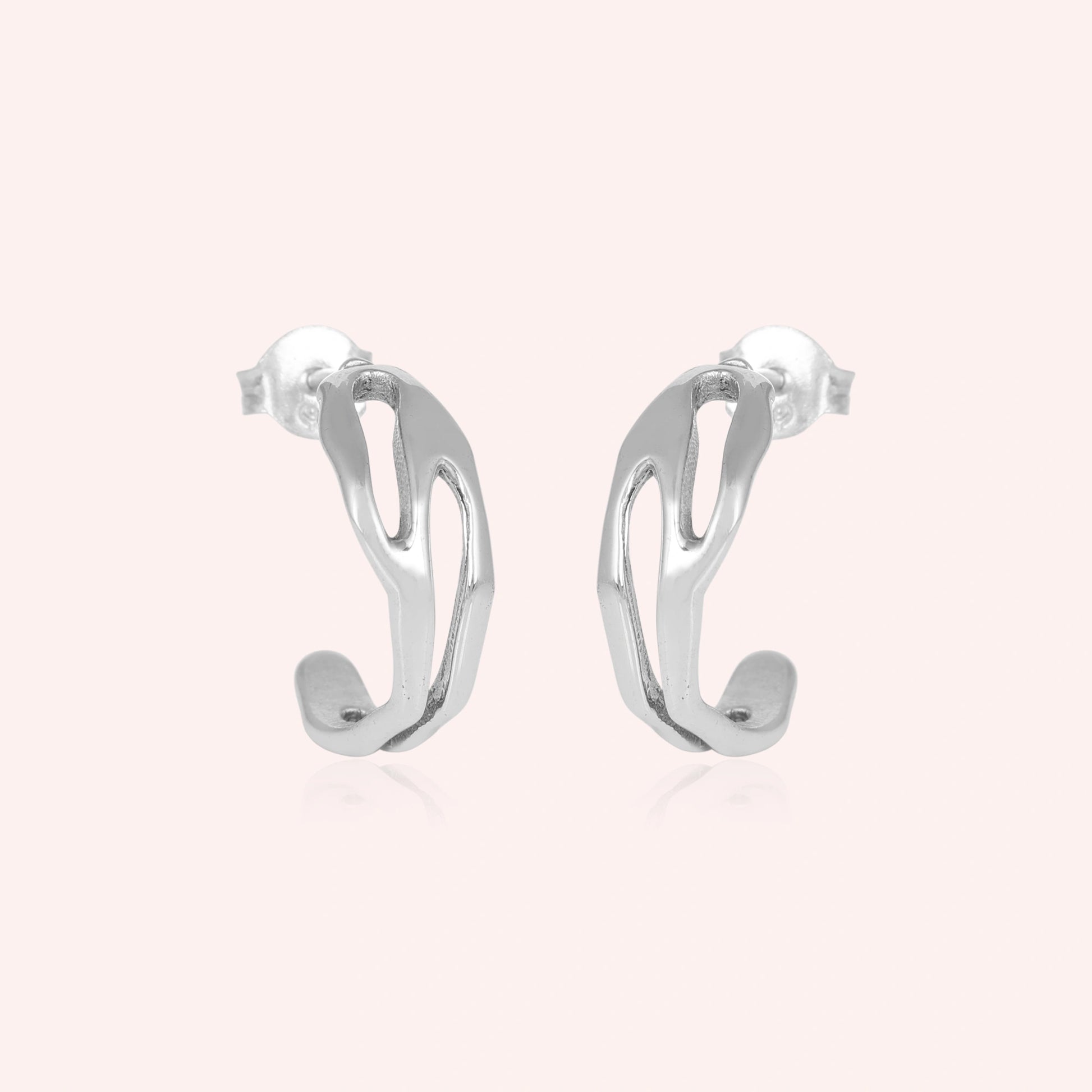 Silver hoop earrings shown at front angled view featuring sleek sculpted open hoops in polished silver against pink background
