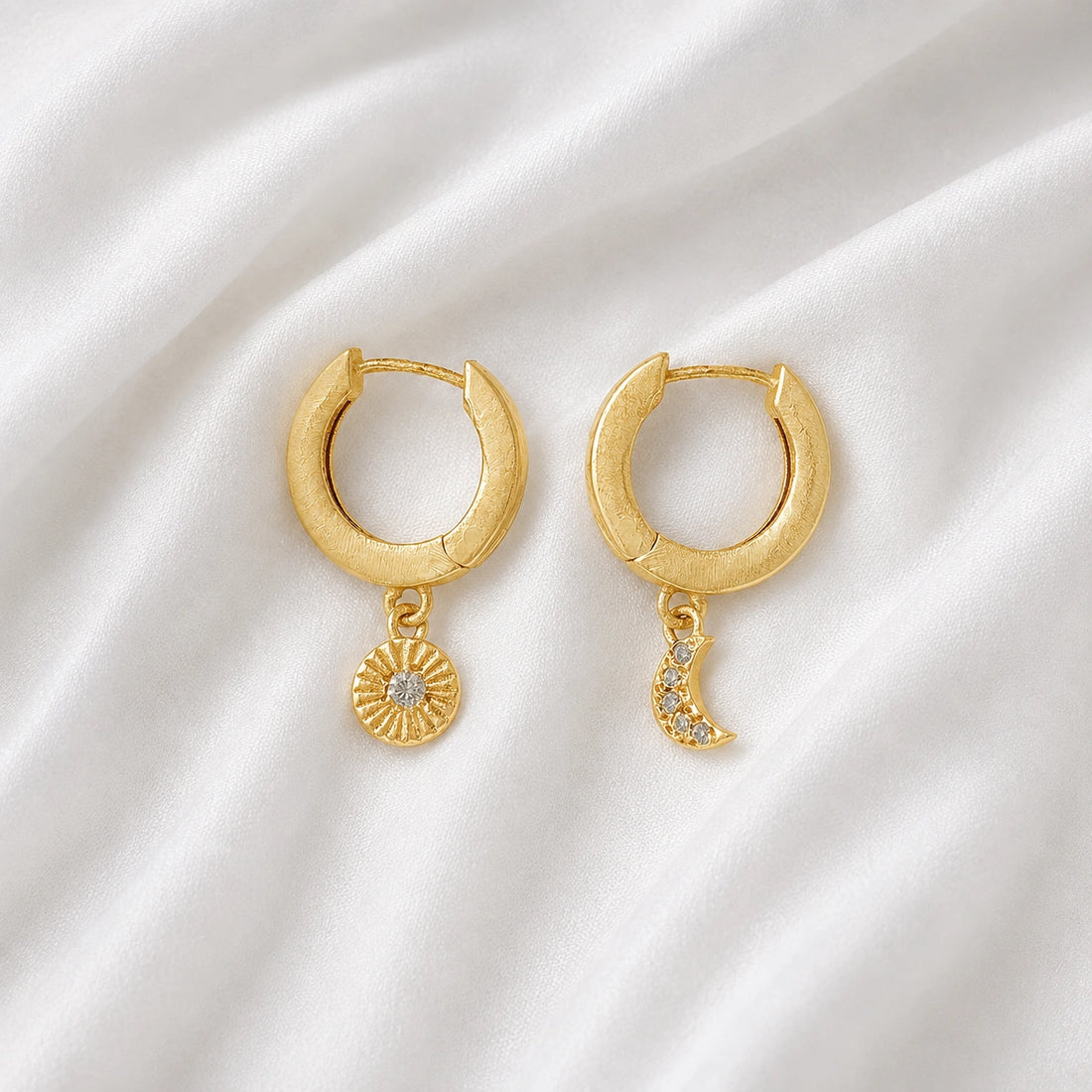 Silver_hoop_earrings_in_gold_plated_silver_with_sun_and_moon_charms_at_front_angle_view_on_soft_fabric_background